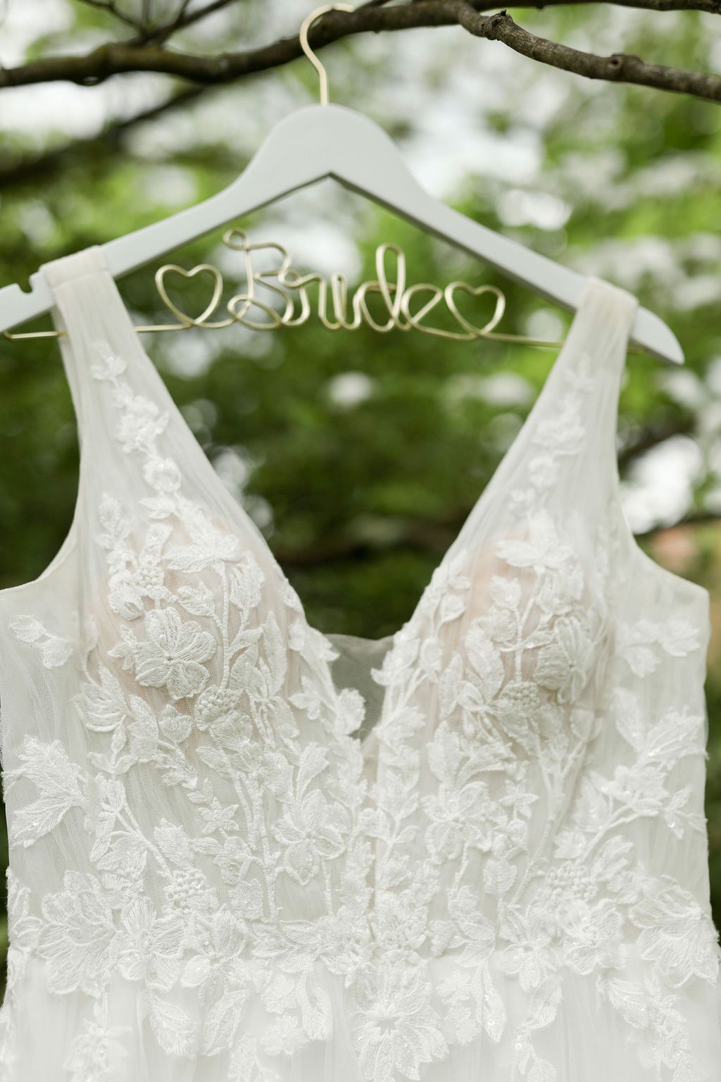 A wedding dress is hanging on a white hanger with the word bride written on it.