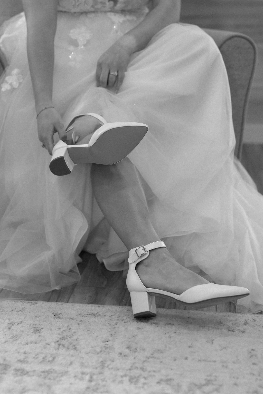 A woman in a wedding dress is tying her shoes in a black and white photo.
