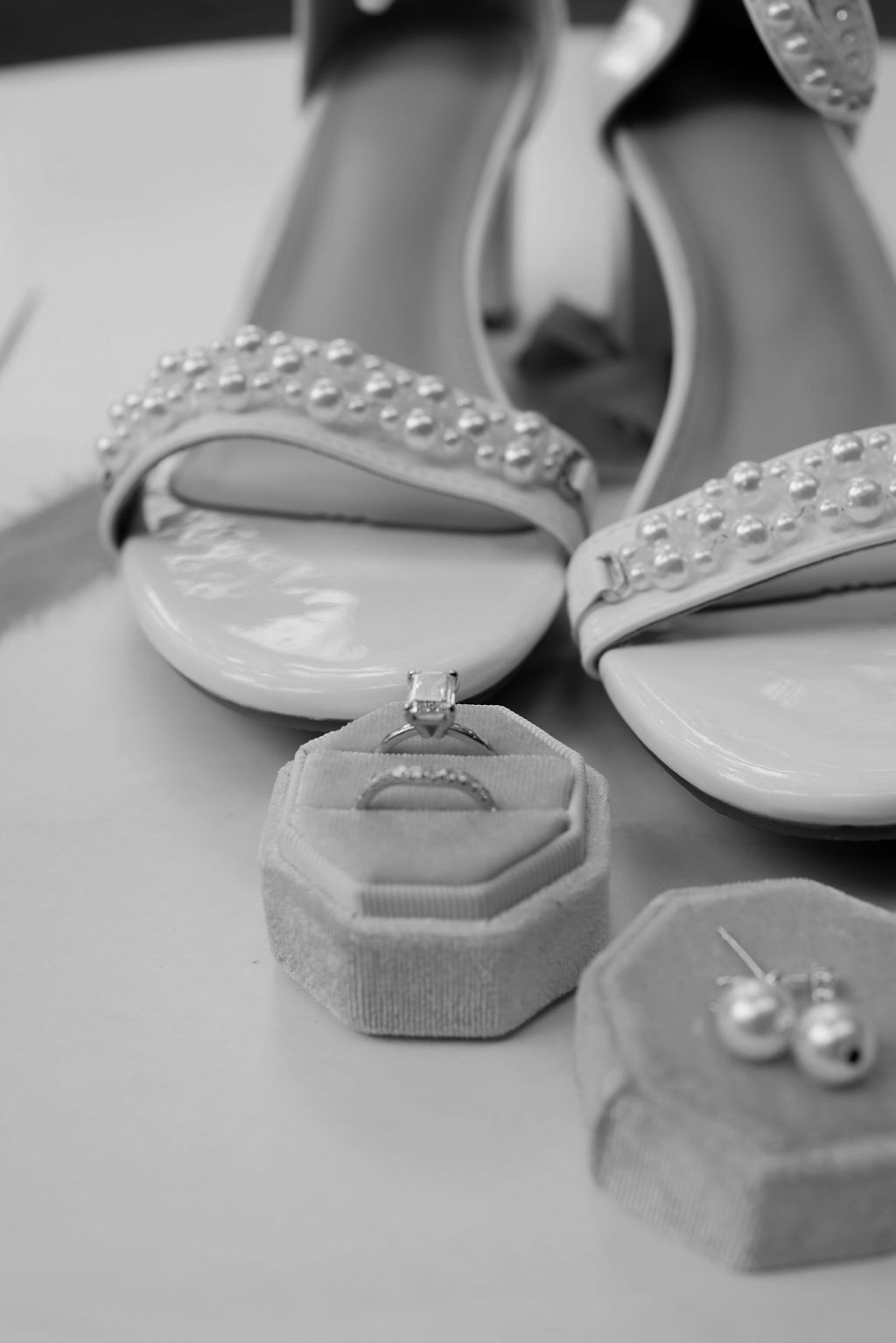 A black and white photo of a bride 's wedding shoes , rings , and earrings.