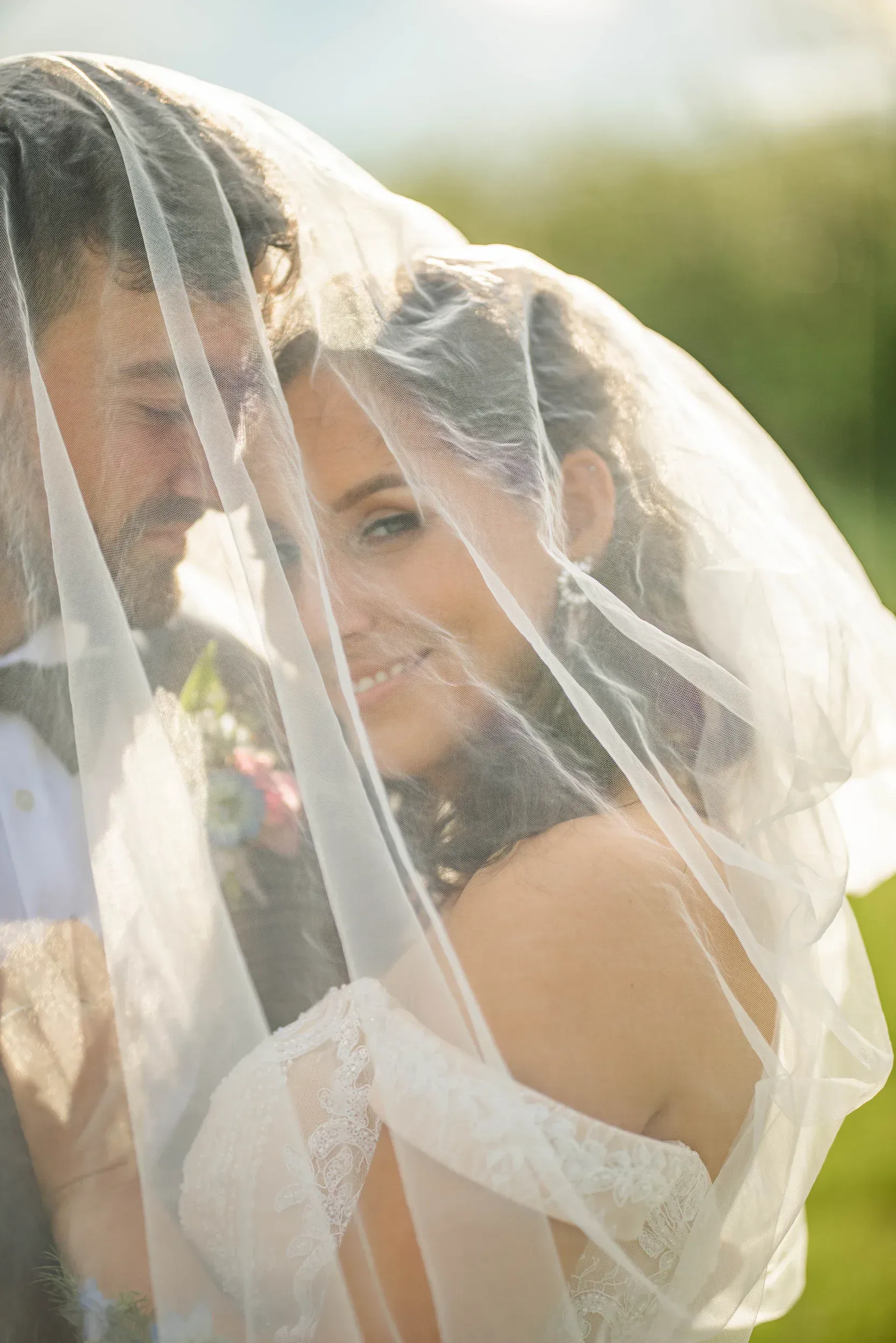 A bride and groom are posing for a picture under a veil.
