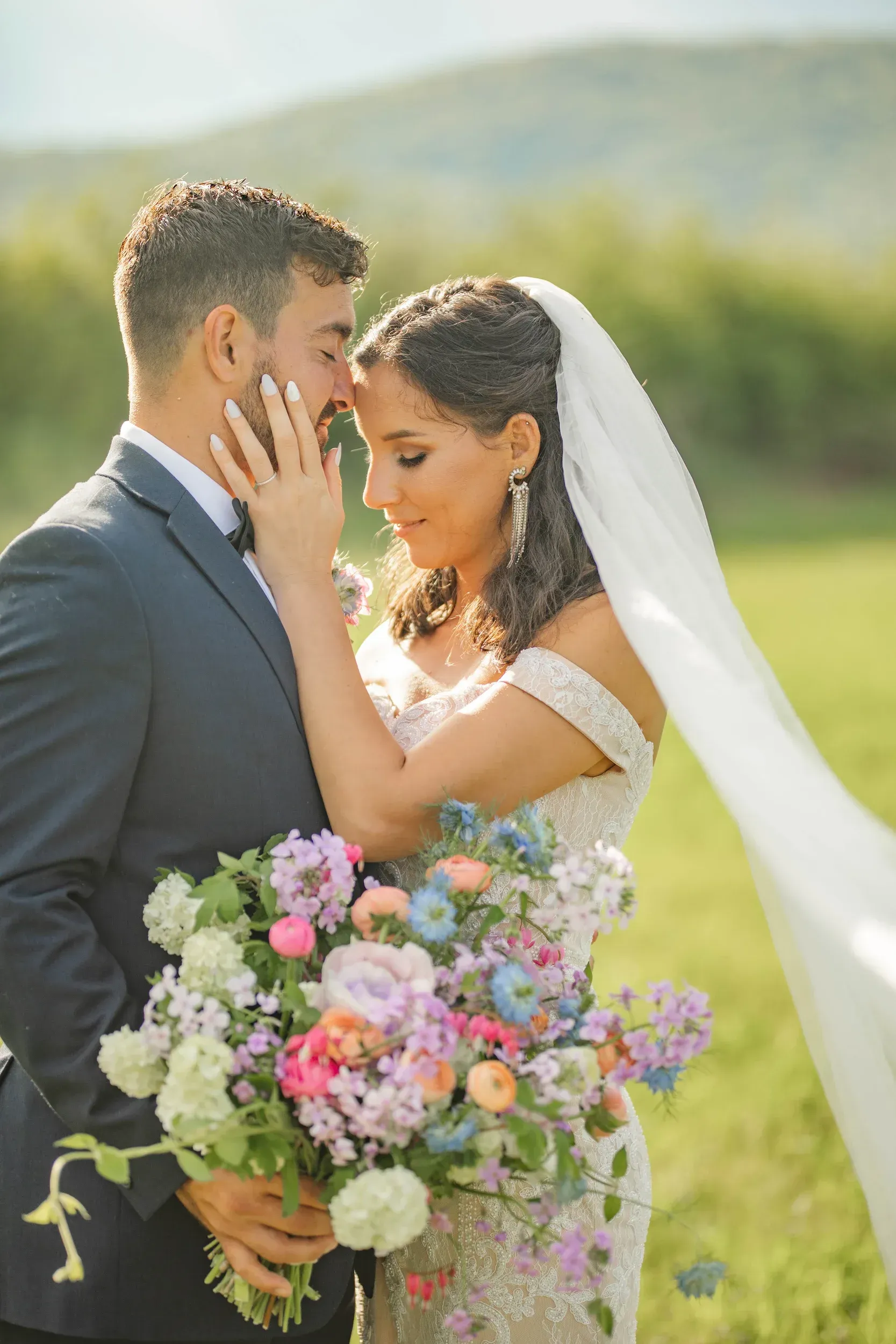 A bride and groom are standing in a field holding a bouquet of flowers.