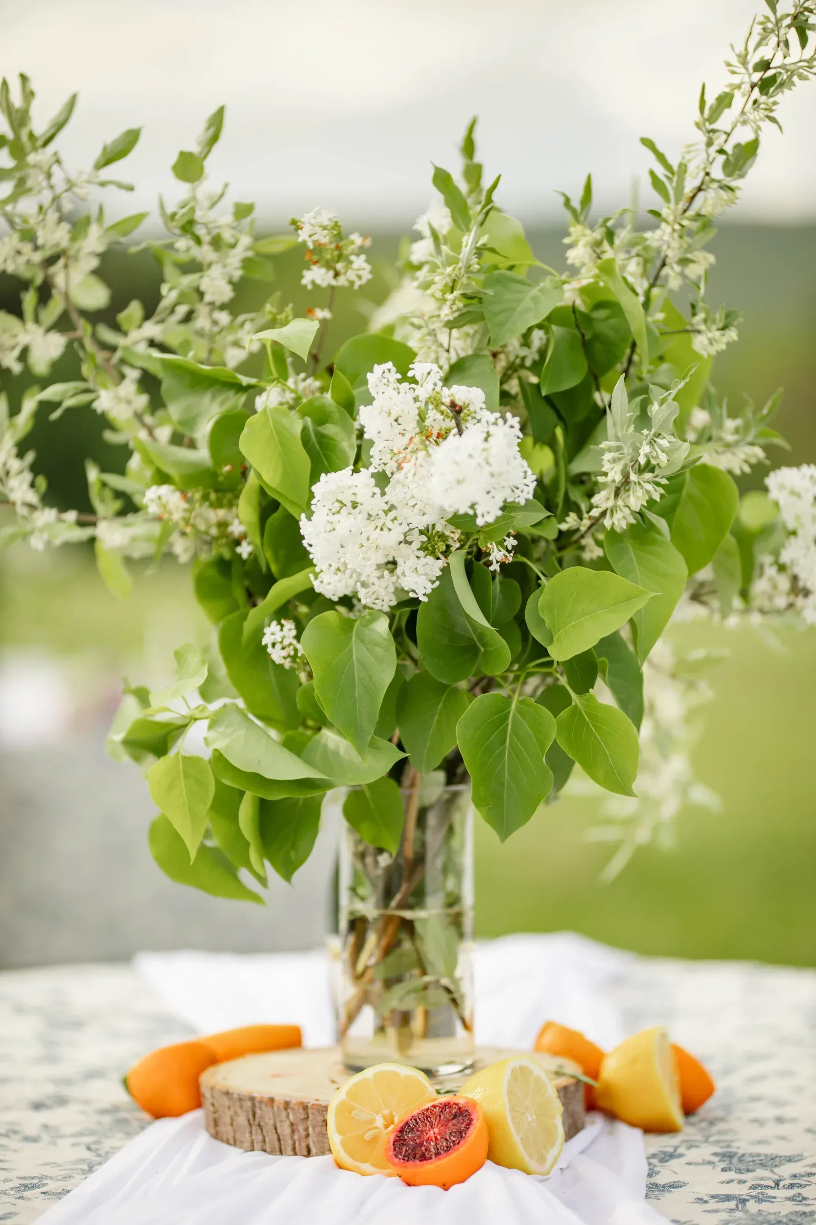 A vase filled with flowers and fruit on a table.