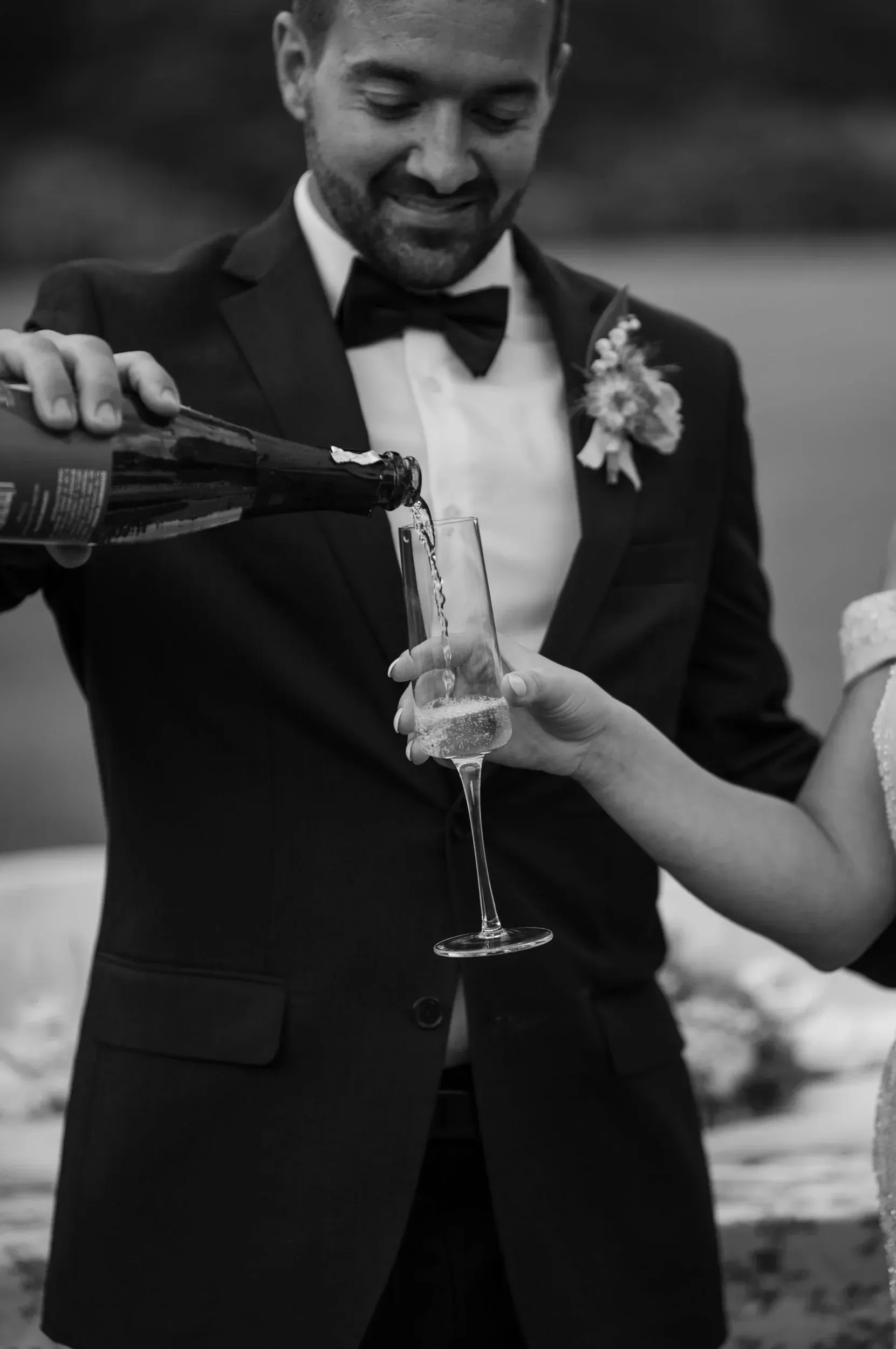 A bride and groom are pouring champagne into a glass.