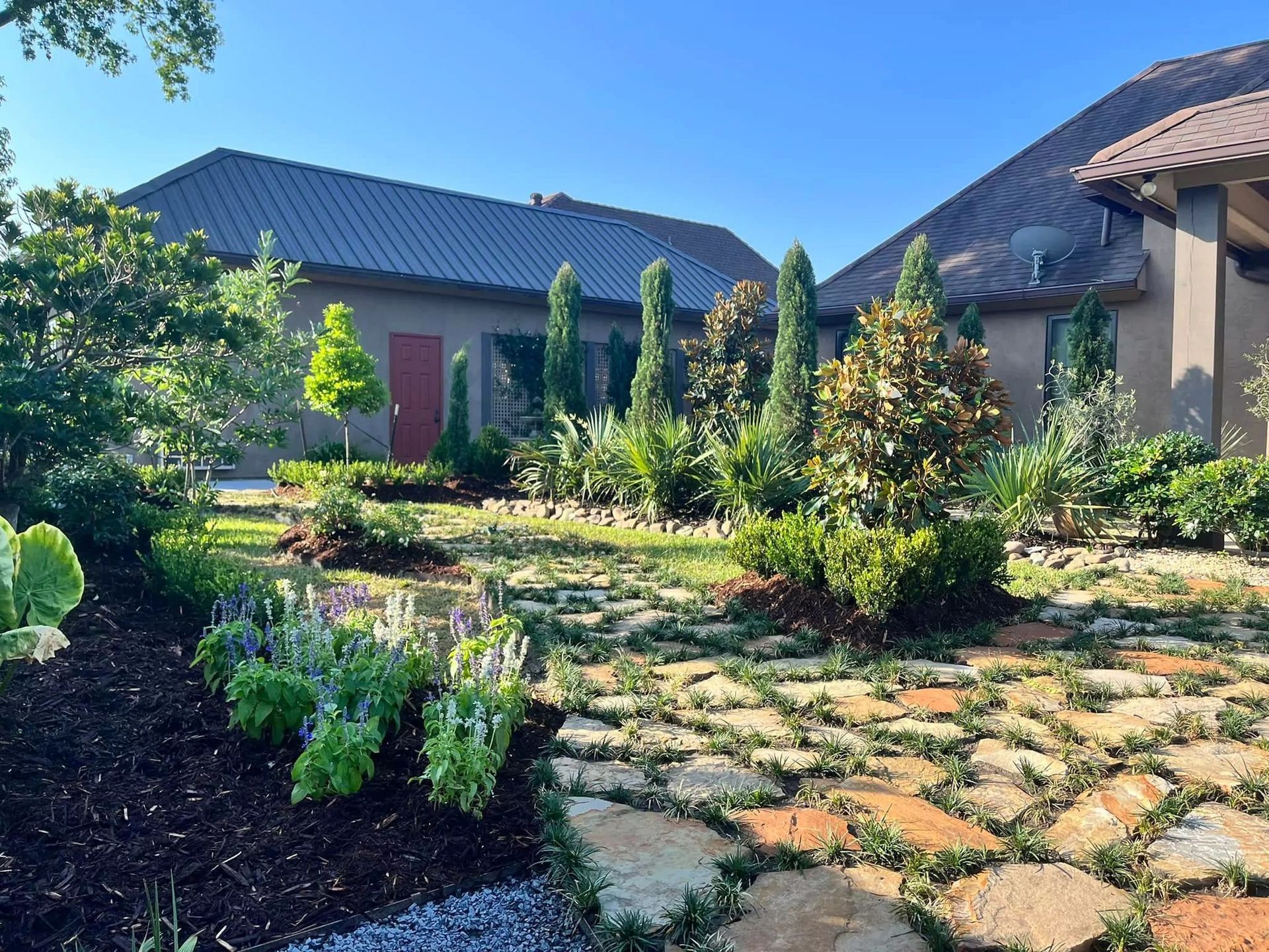 A stone walkway leads to a large house surrounded by trees and bushes.