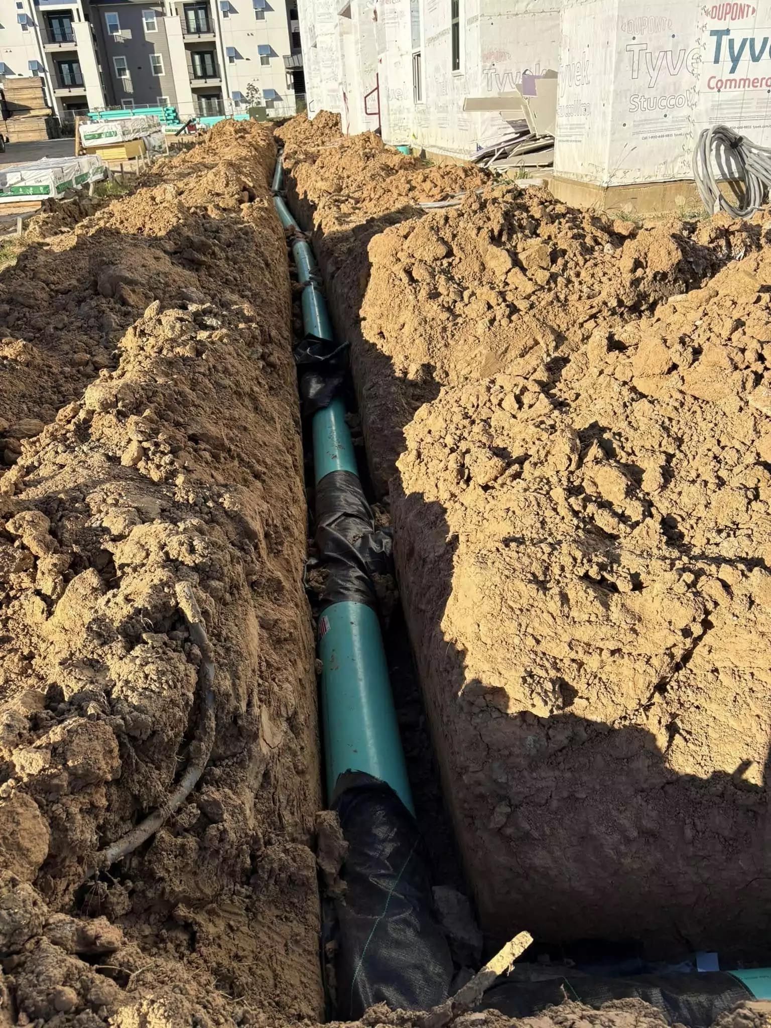 A green pipe is being installed in the dirt.