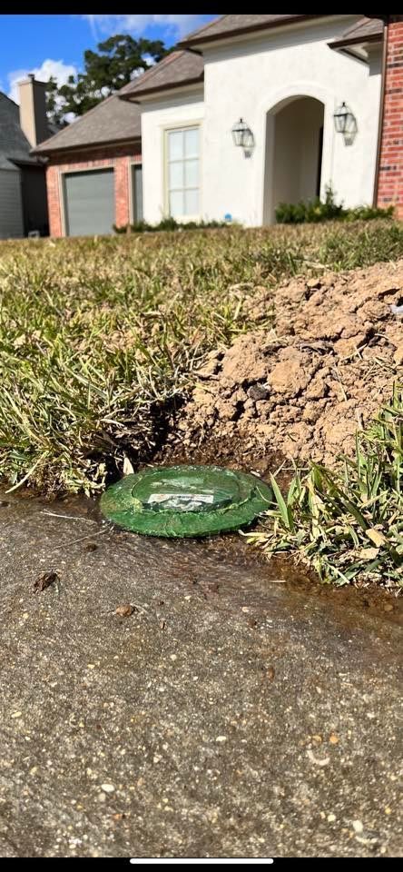 A green manhole cover is sitting on the sidewalk in front of a house.