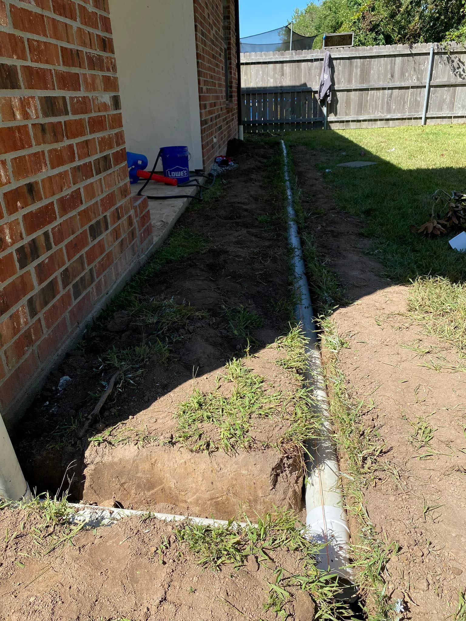 A drain pipe is being installed in the backyard of a house.