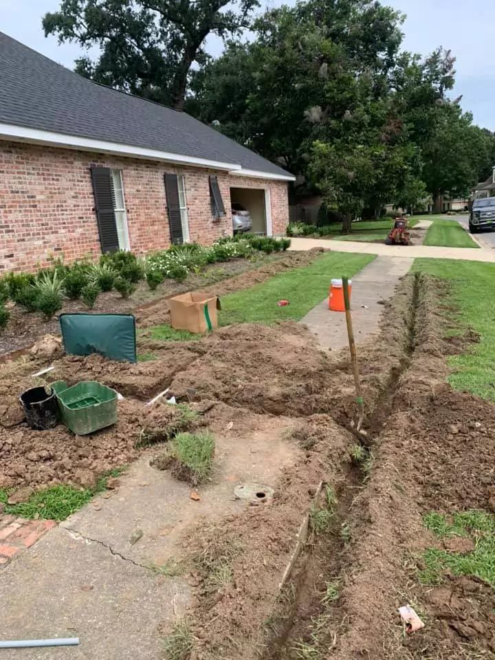A drainage system is being installed in front of a brick house.