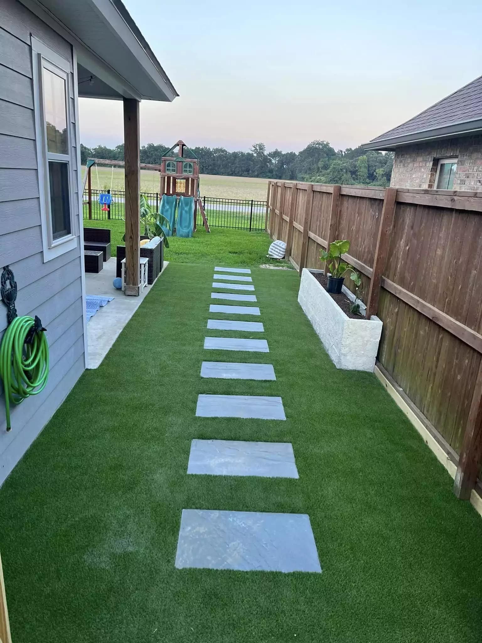 A walkway leading to a house with a playground in the background.