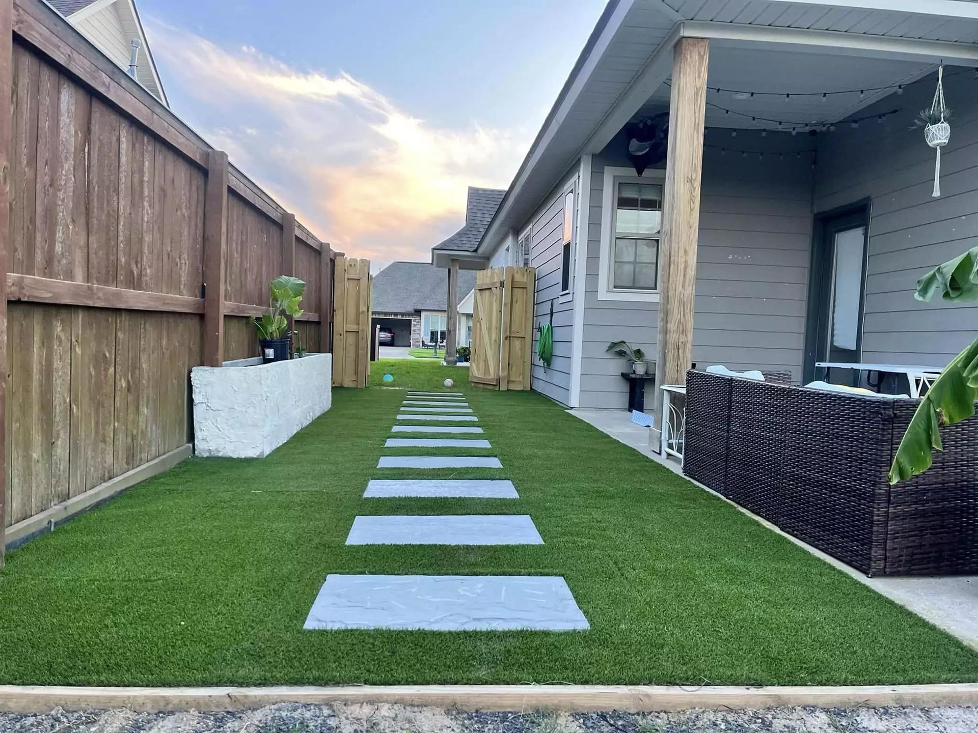 A walkway leading to a house with a wooden fence and grass.