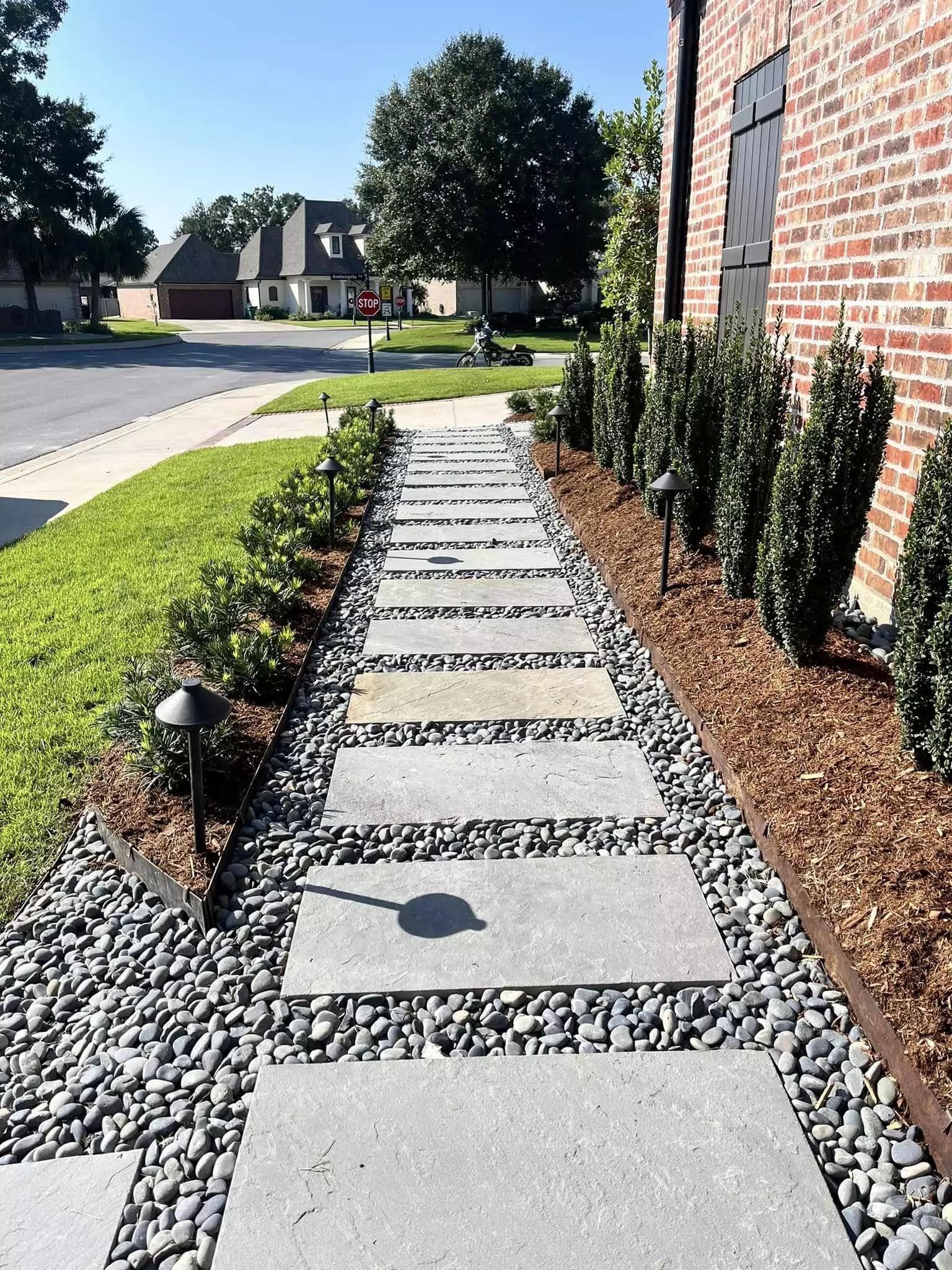 A stone walkway leading to a brick house in a residential neighborhood.