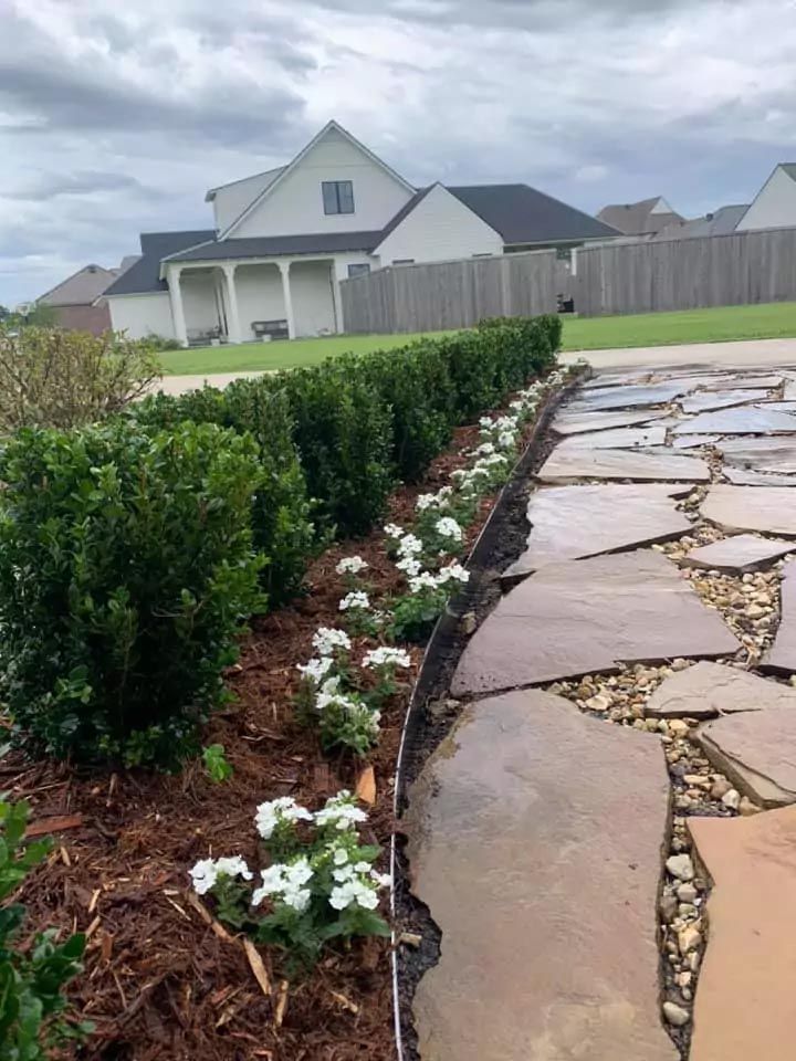A stone walkway leading to a house with flowers in the foreground.