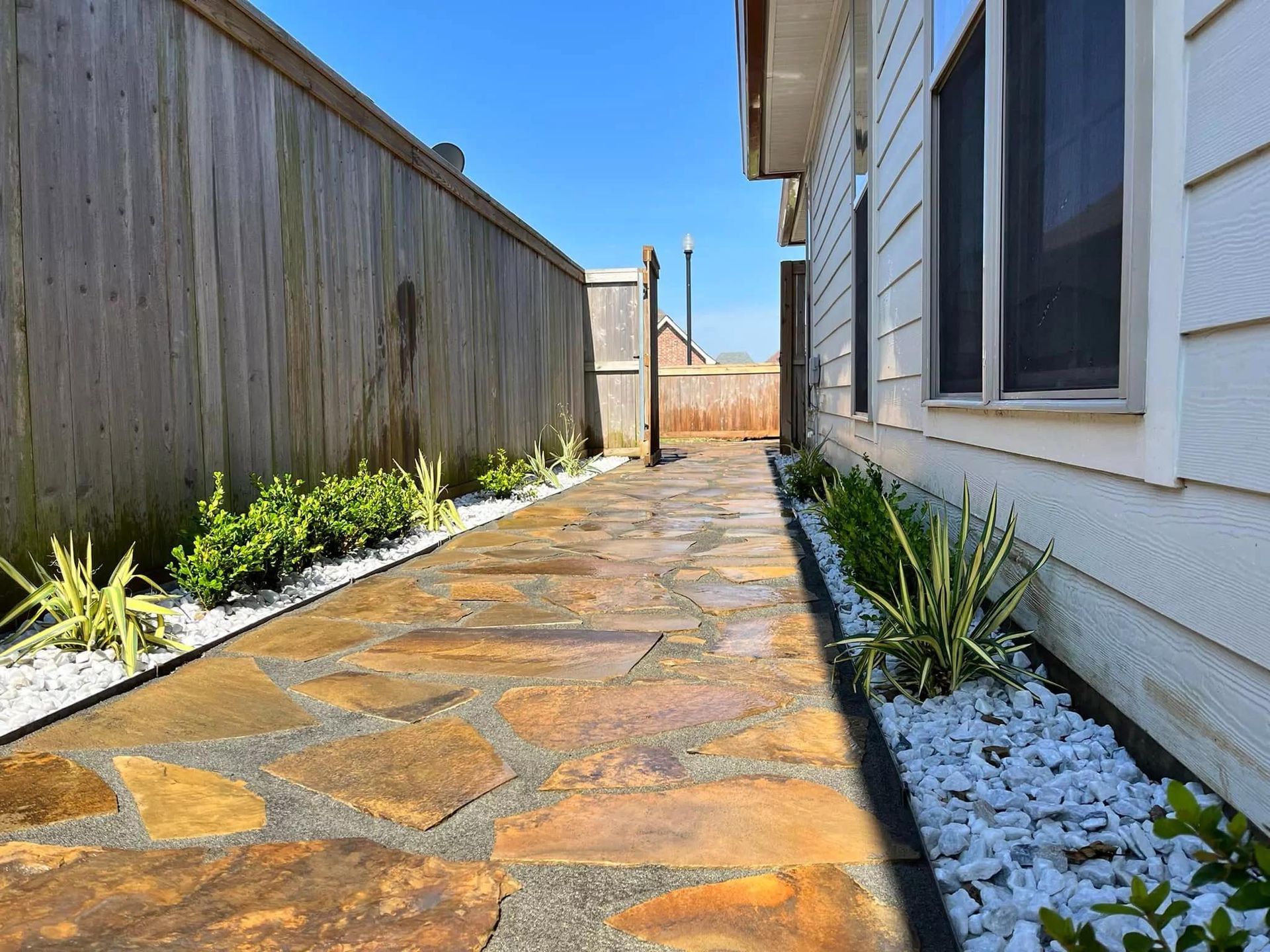 A stone walkway leading to a house with a wooden fence.