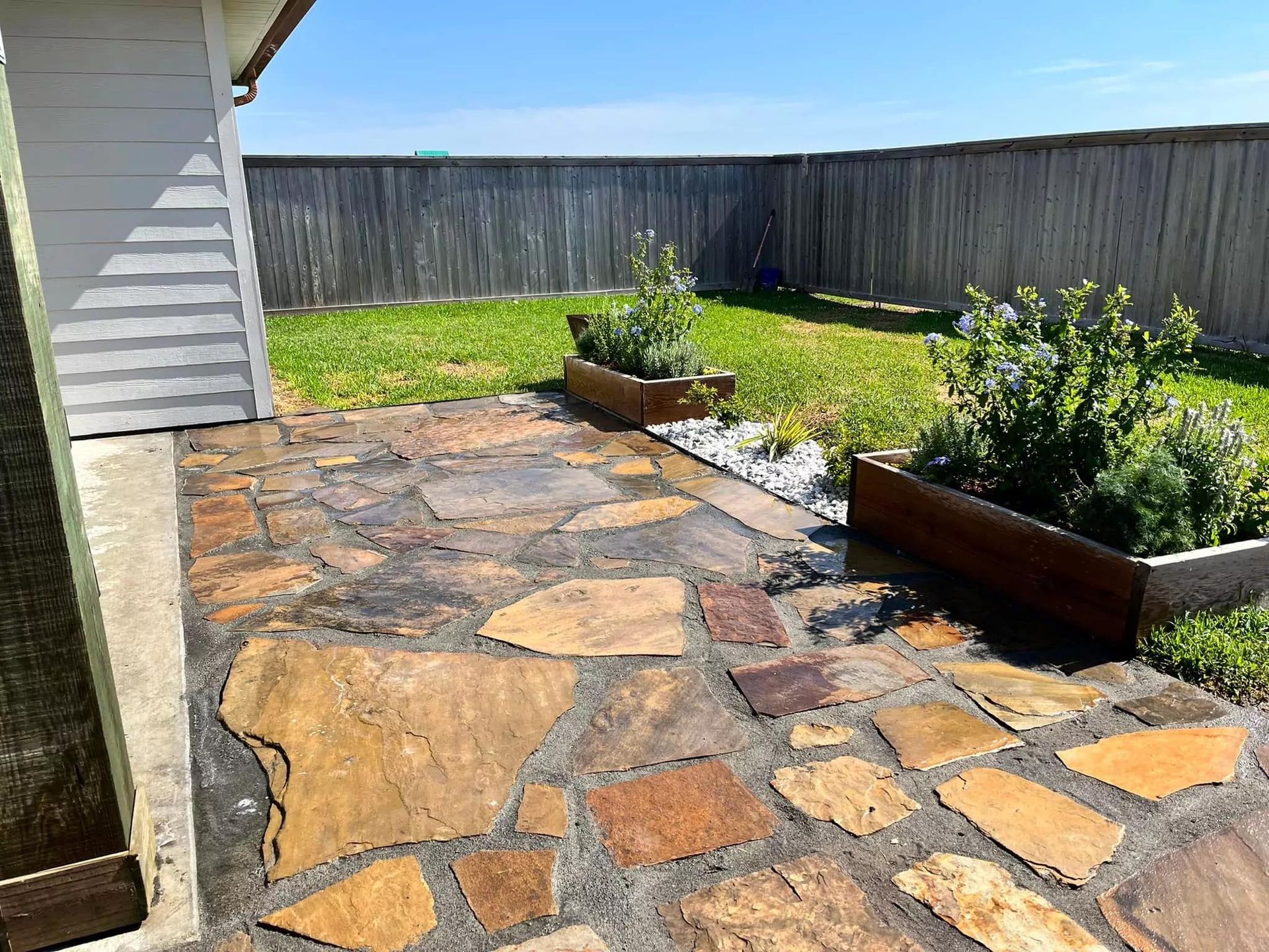 A backyard with a stone patio and a wooden fence.
