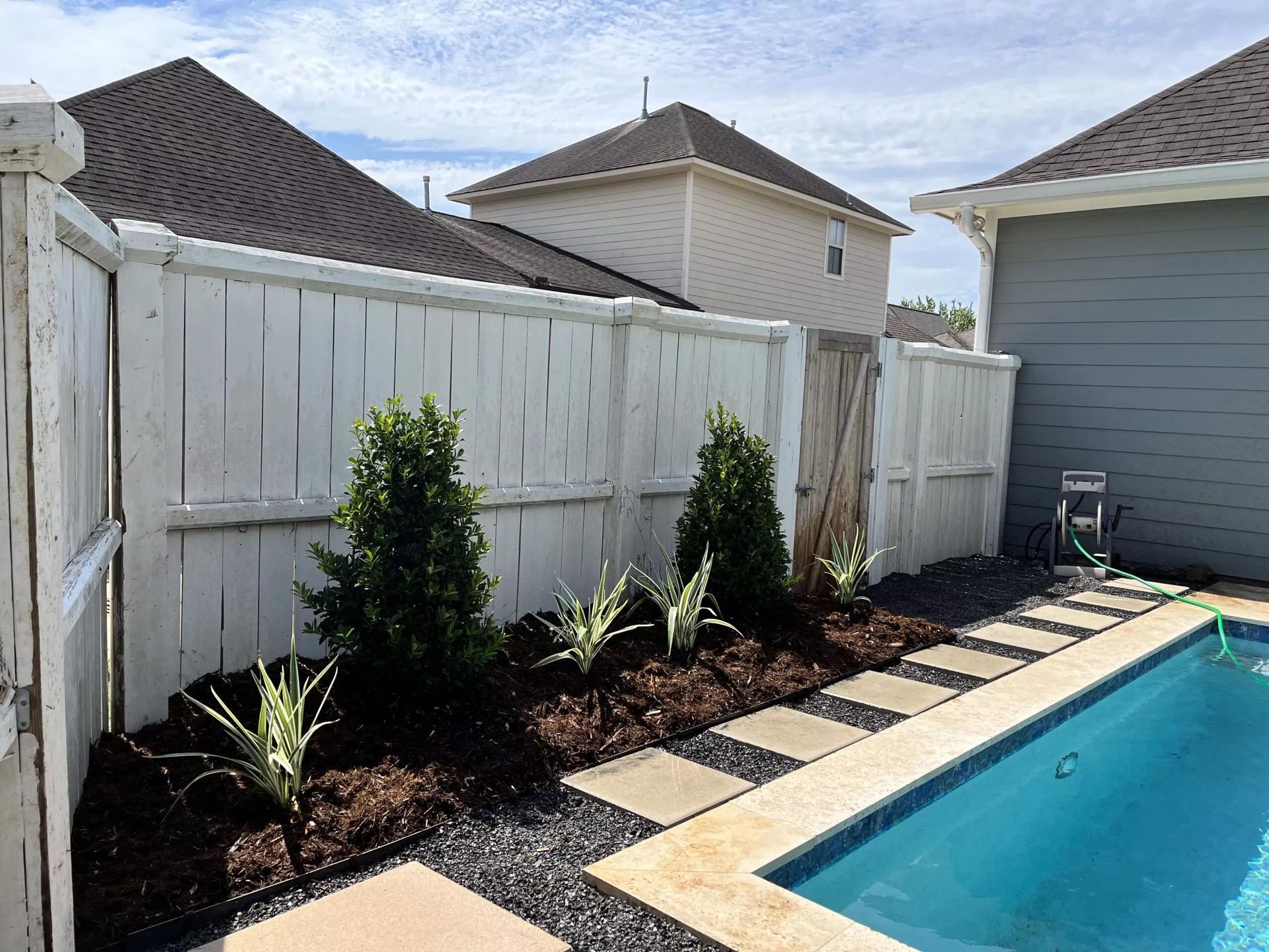 A white fence surrounds a swimming pool in a backyard.