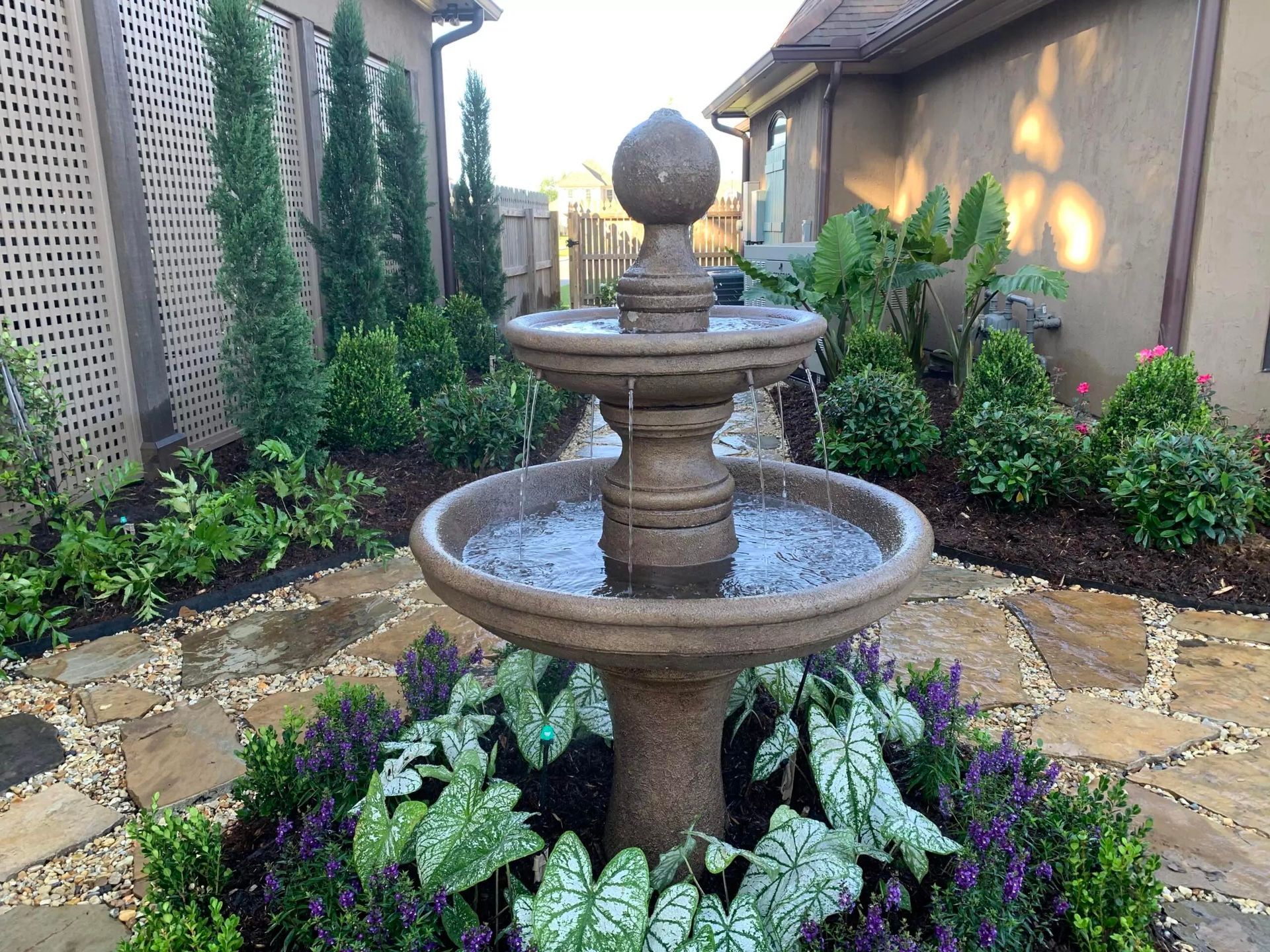 A fountain is surrounded by flowers and plants in a garden.
