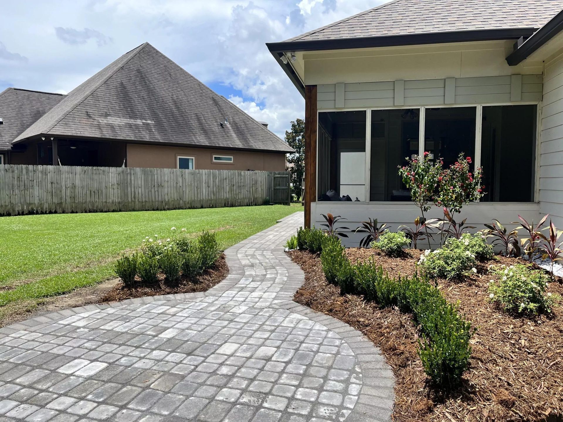 A brick walkway leading to a house with a screened in porch.