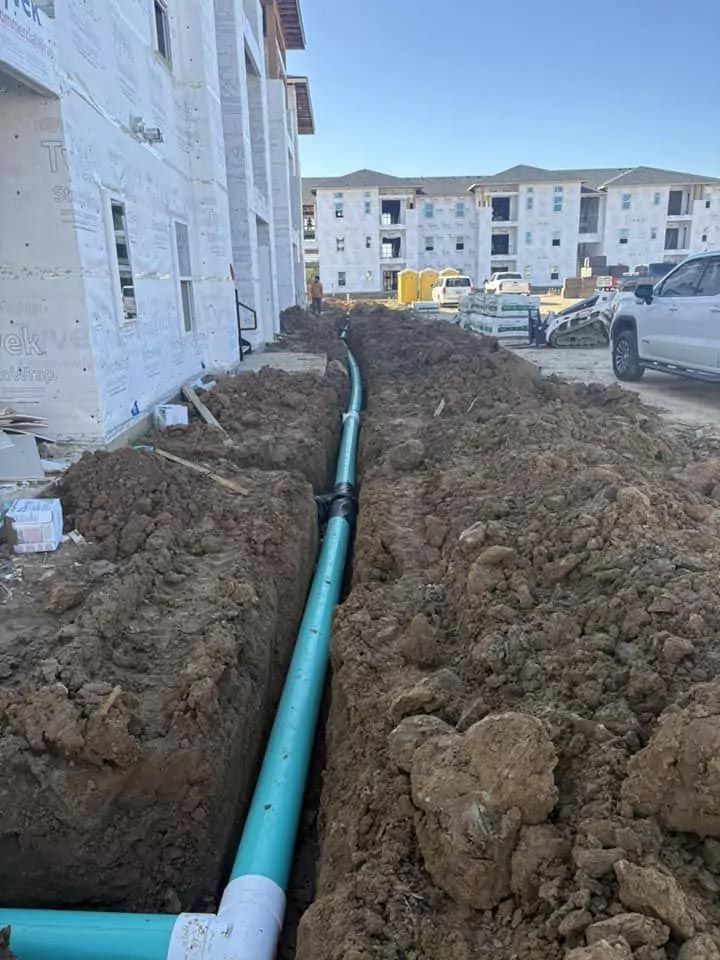 A green pipe is being installed in the dirt in front of a building under construction.