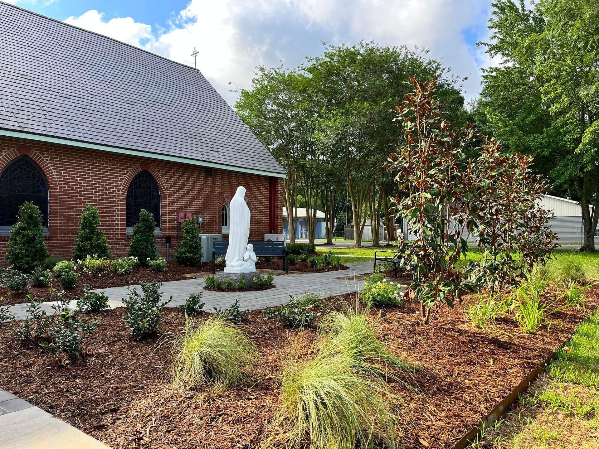 There is a statue of jesus in the middle of a garden in front of a church.