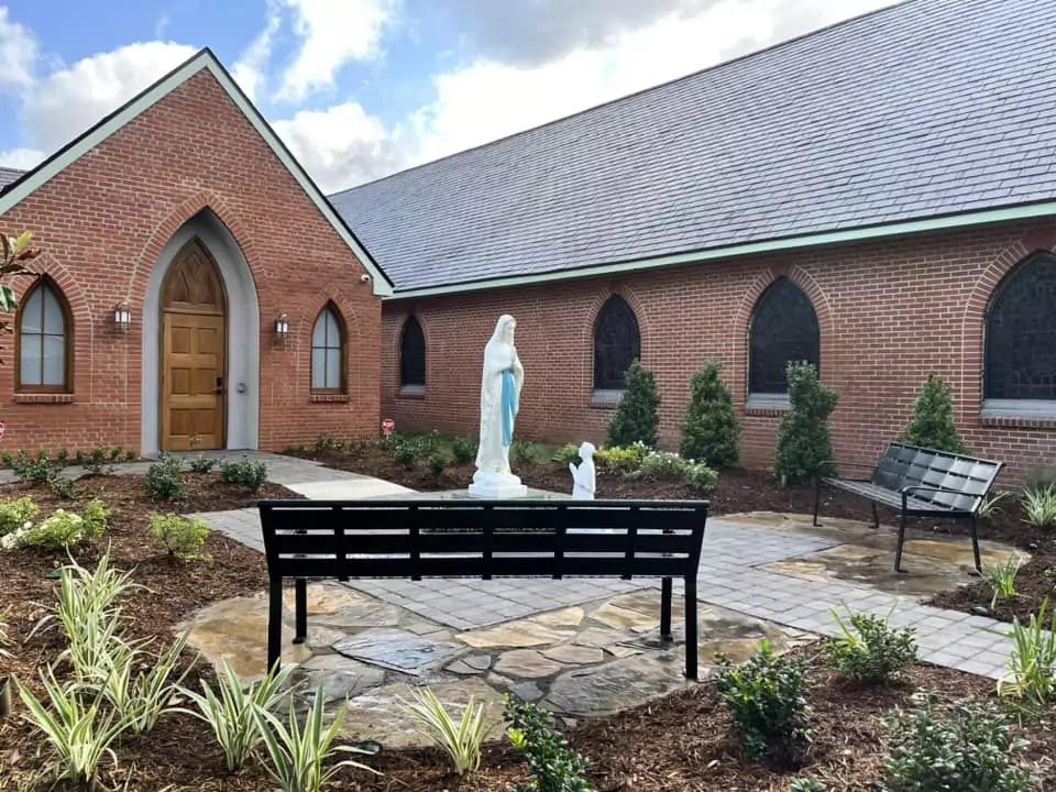 A statue of mary is sitting on a bench in front of a church.