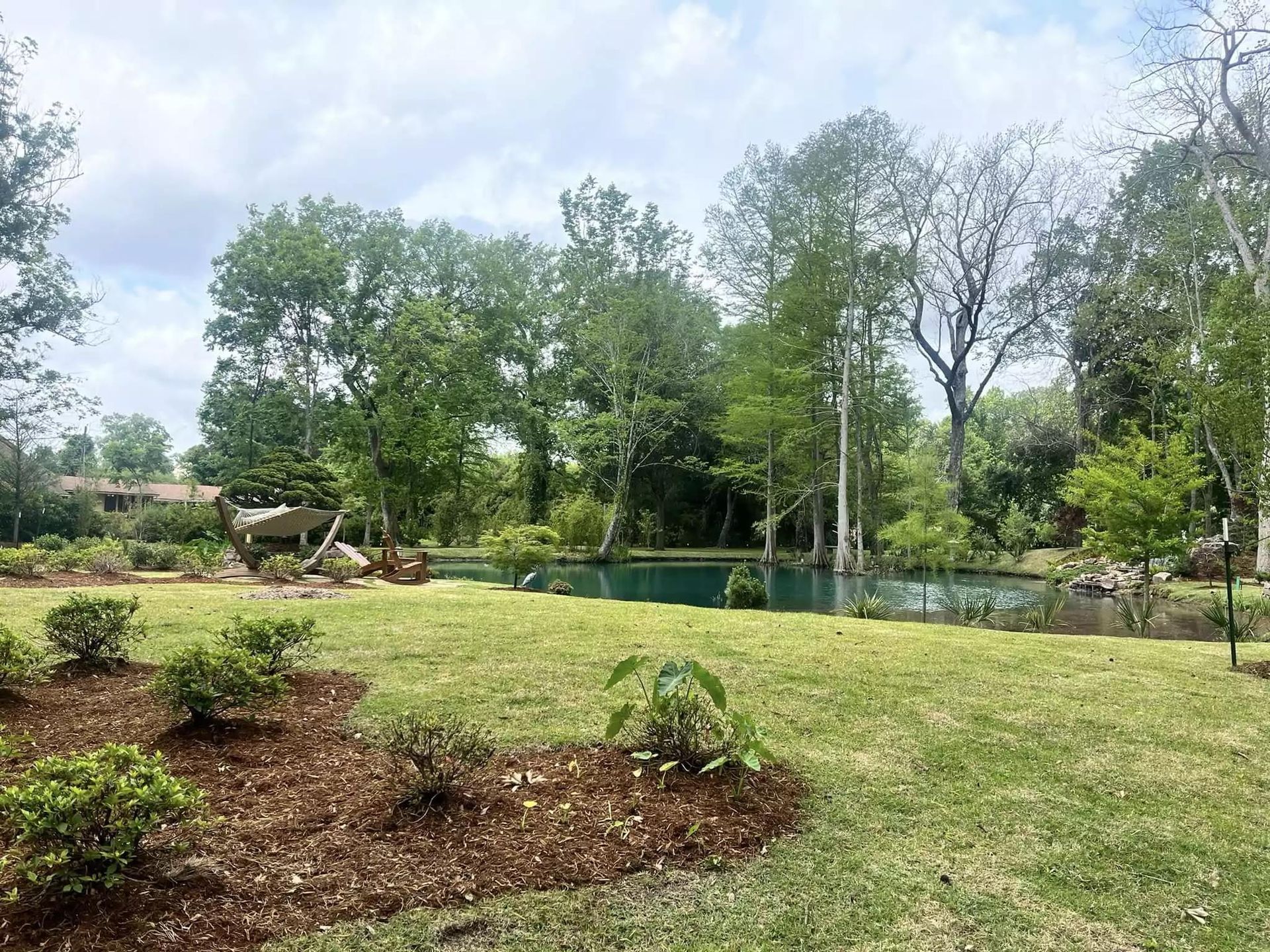 A large lush green field with trees and a pond in the background.