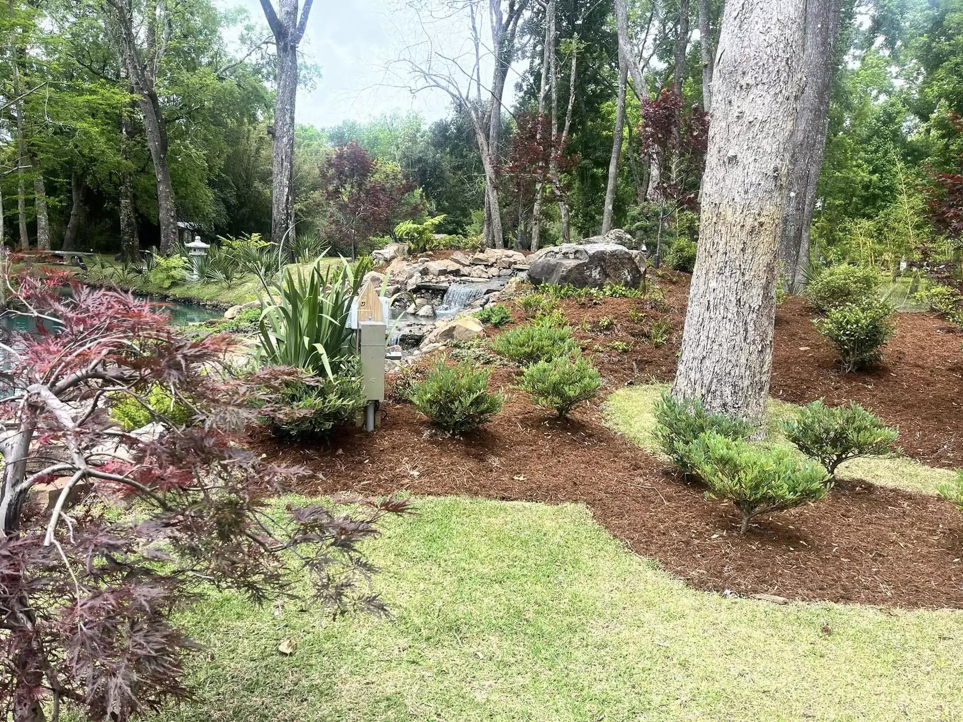 There is a waterfall in the middle of the garden surrounded by trees.