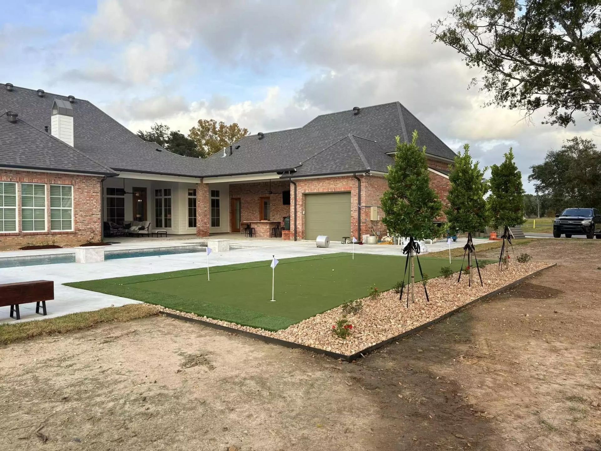 A large brick house with a swimming pool and a putting green in front of it.