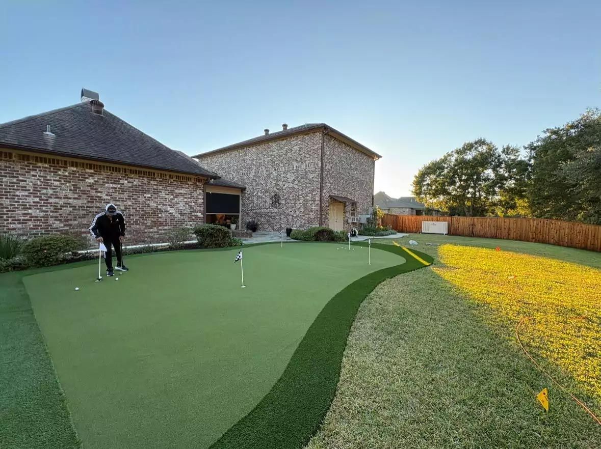 A man is playing golf on a putting green in front of a house.