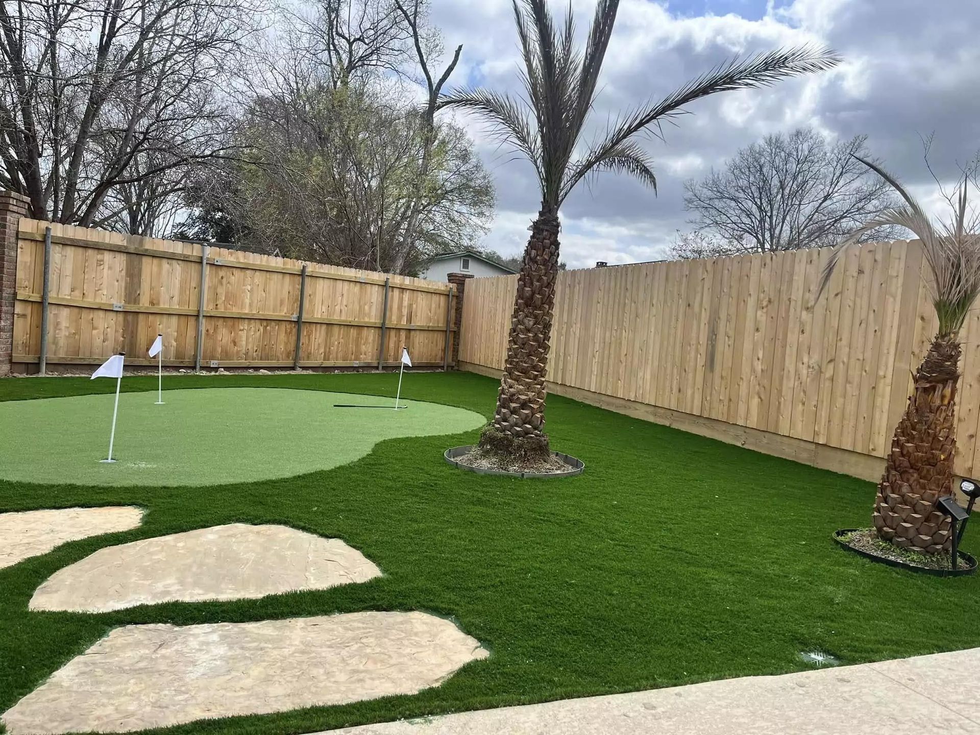 A backyard with a putting green and a wooden fence.
