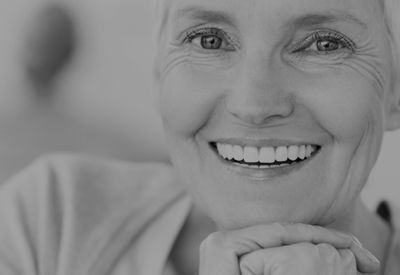 A black and white photo of an older woman smiling with her hands on her chin.