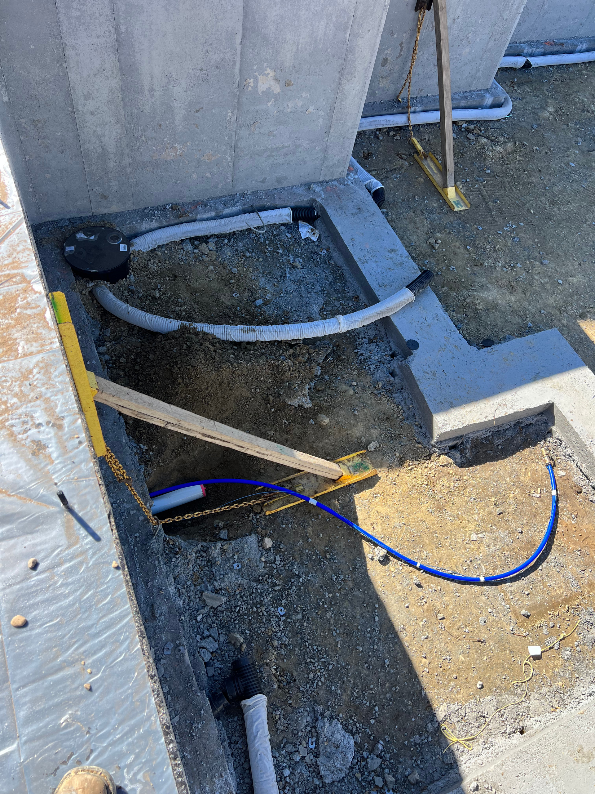 A bunch of pipes are laying in the dirt next to a wall.