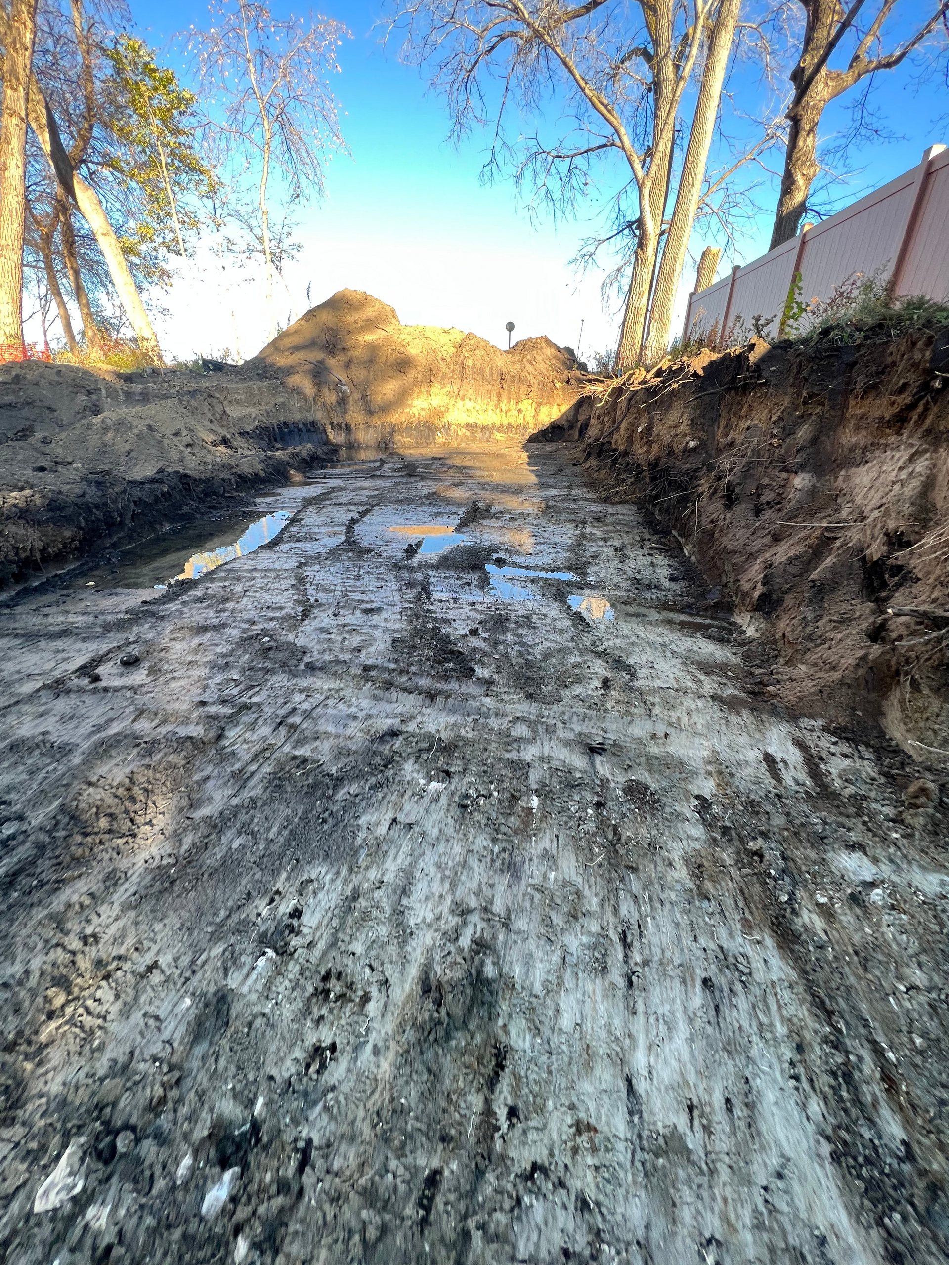 A muddy dirt road with trees in the background.