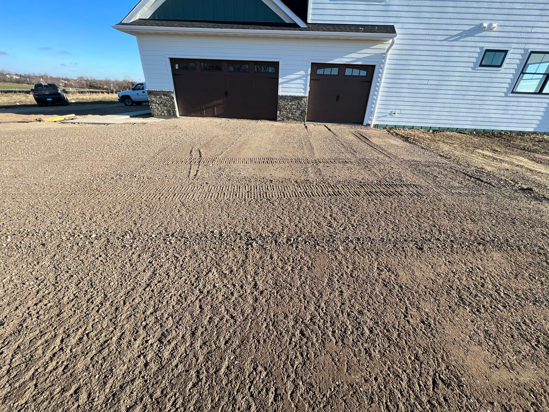 A white house with two garage doors and a gravel driveway in front of it.