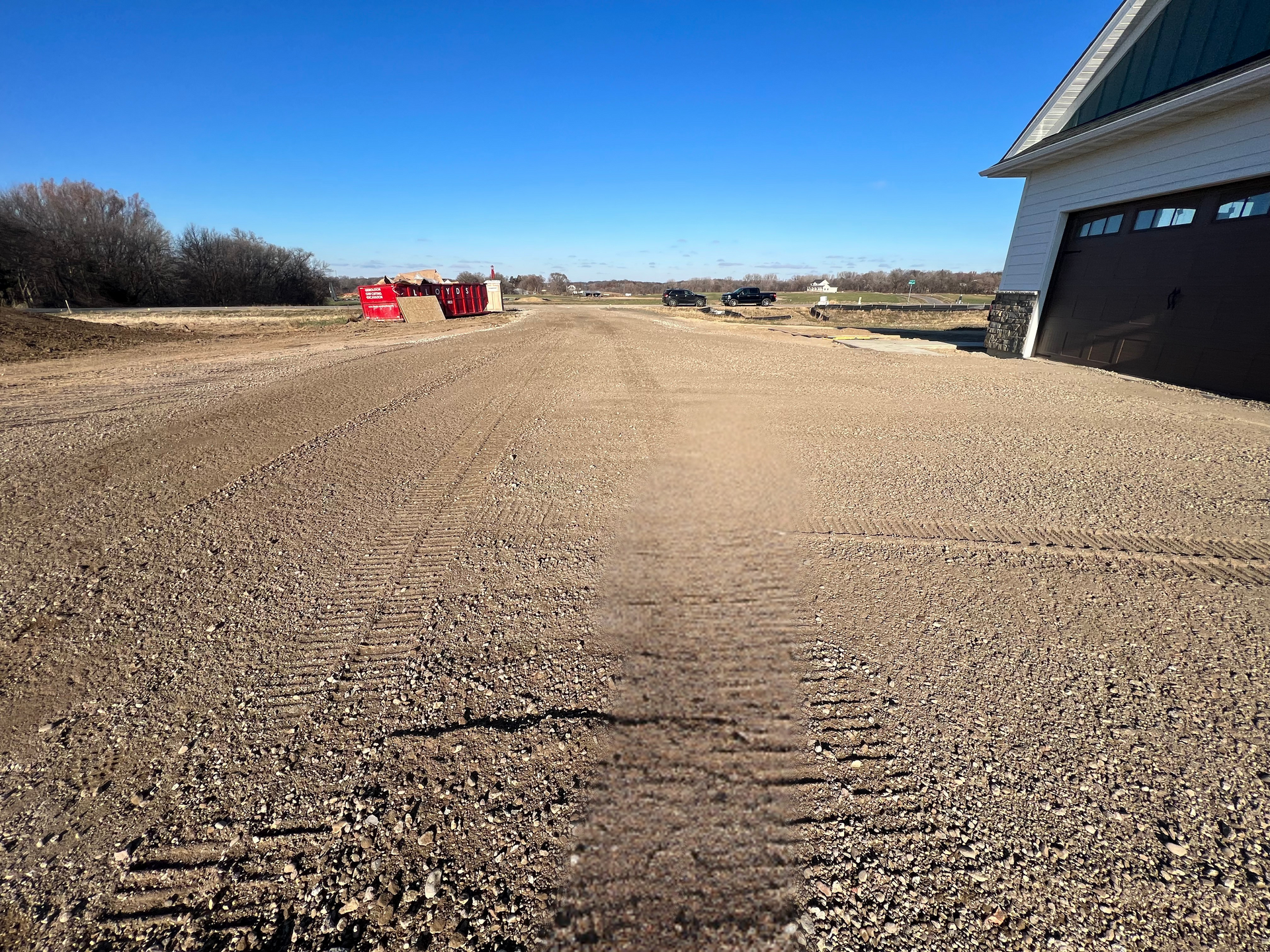 A gravel road leading to a garage with a house in the background.