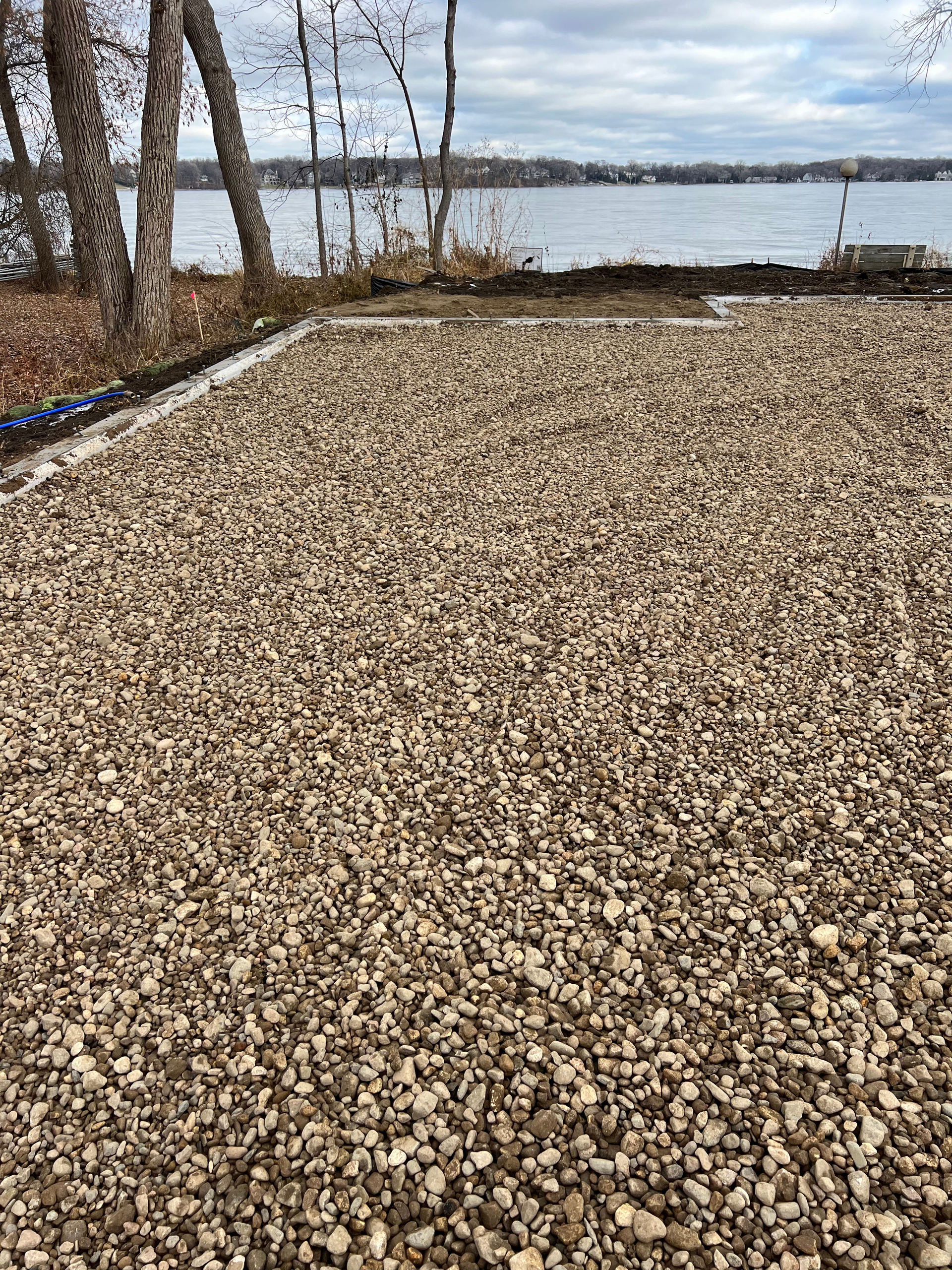 A gravel driveway next to a lake with trees in the background.