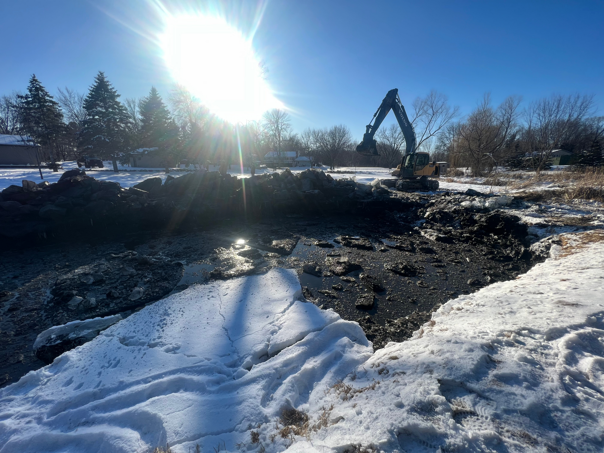 A large excavator is digging a hole in the snow.