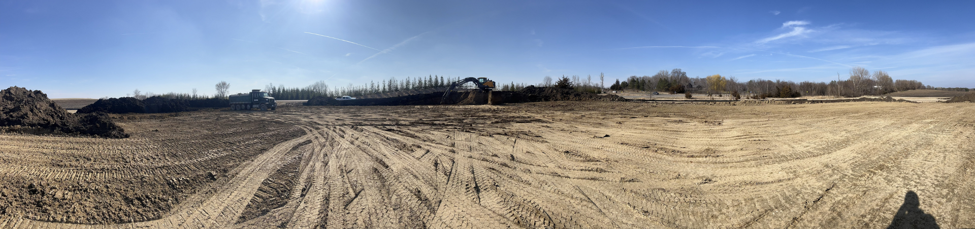 A dirt road going through a field with a blue sky in the background.
