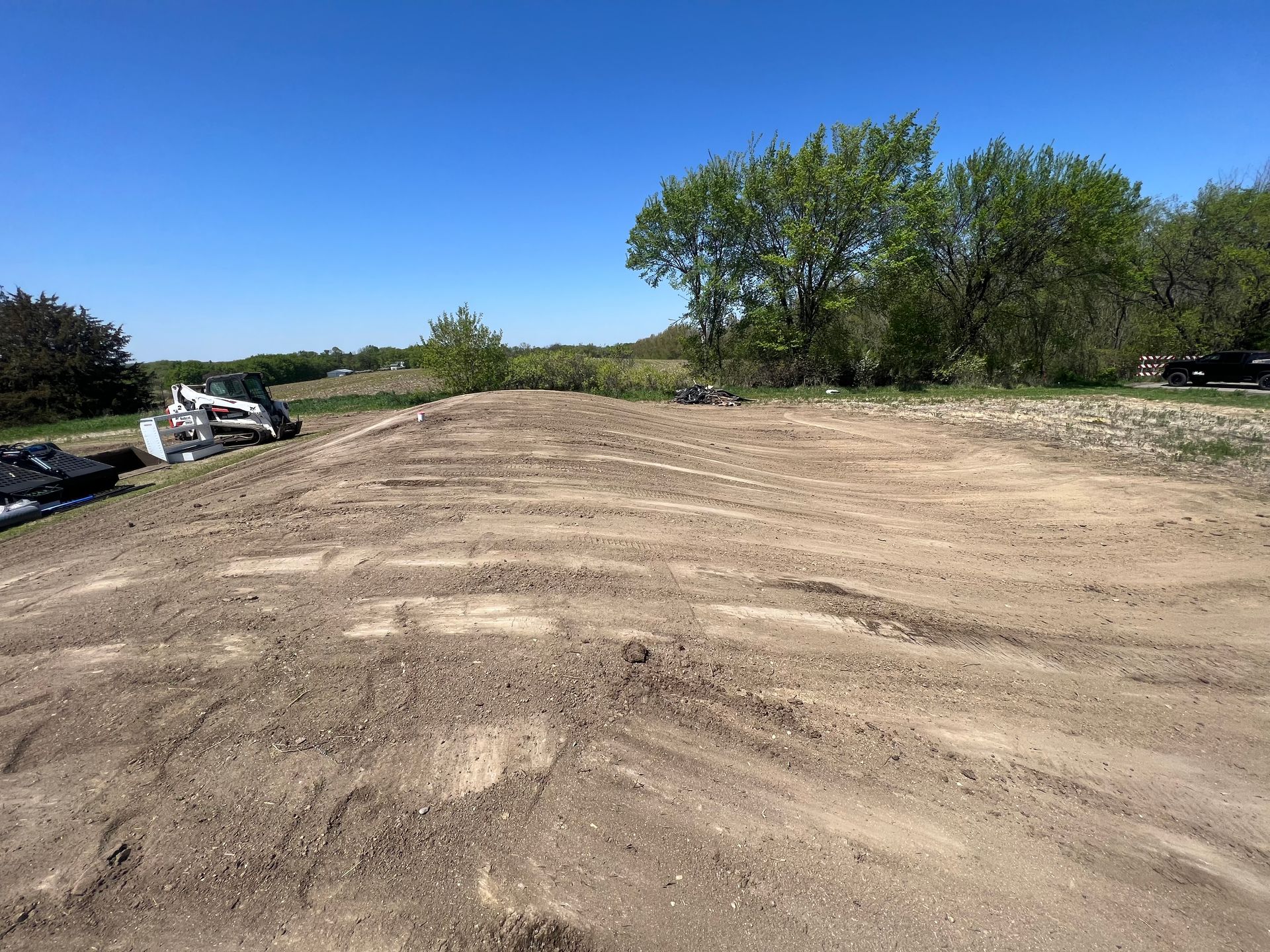 A large dirt field with trees in the background and a bulldozer in the foreground.