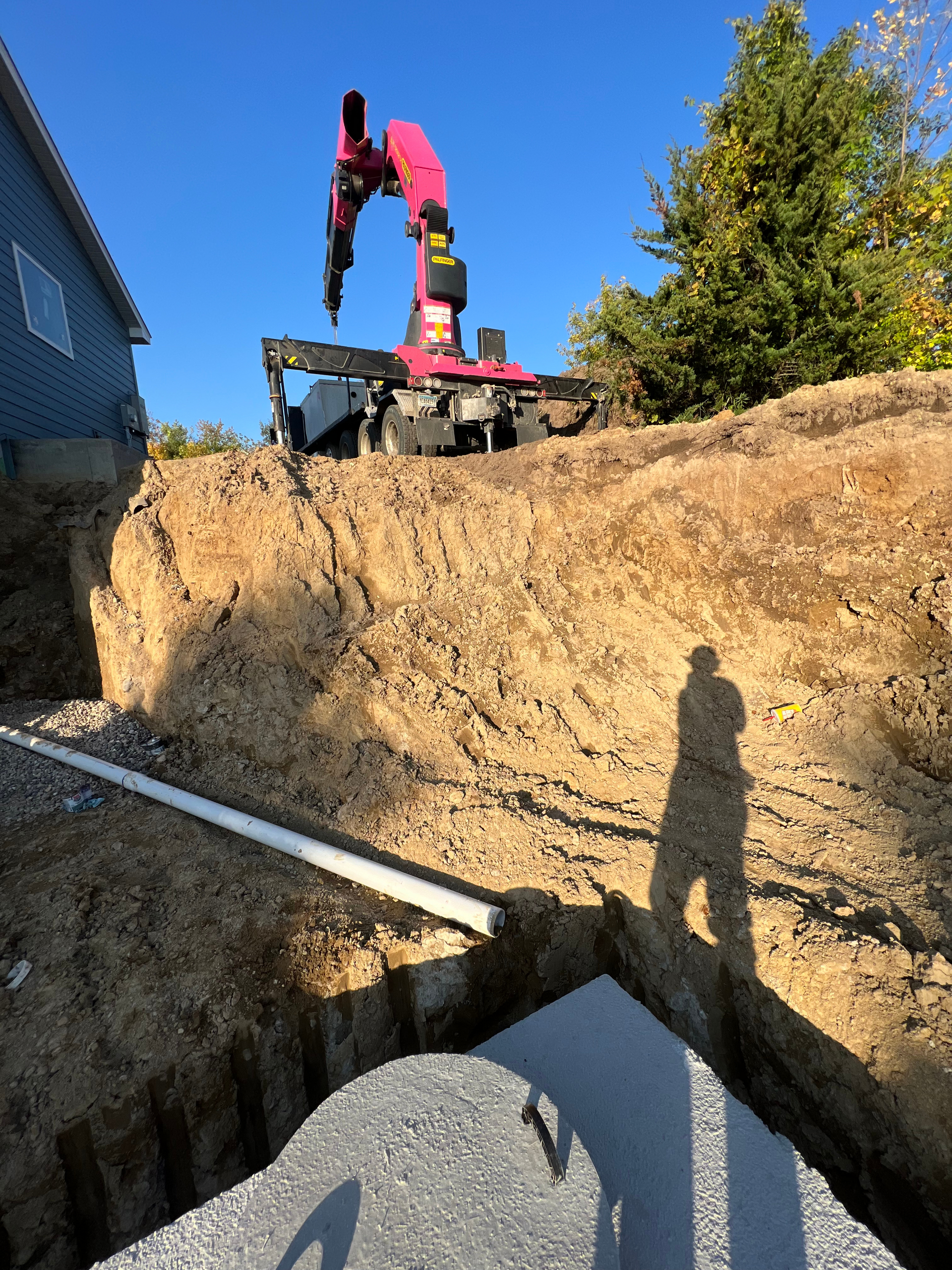 A pink crane is sitting on top of a pile of dirt next to a house.