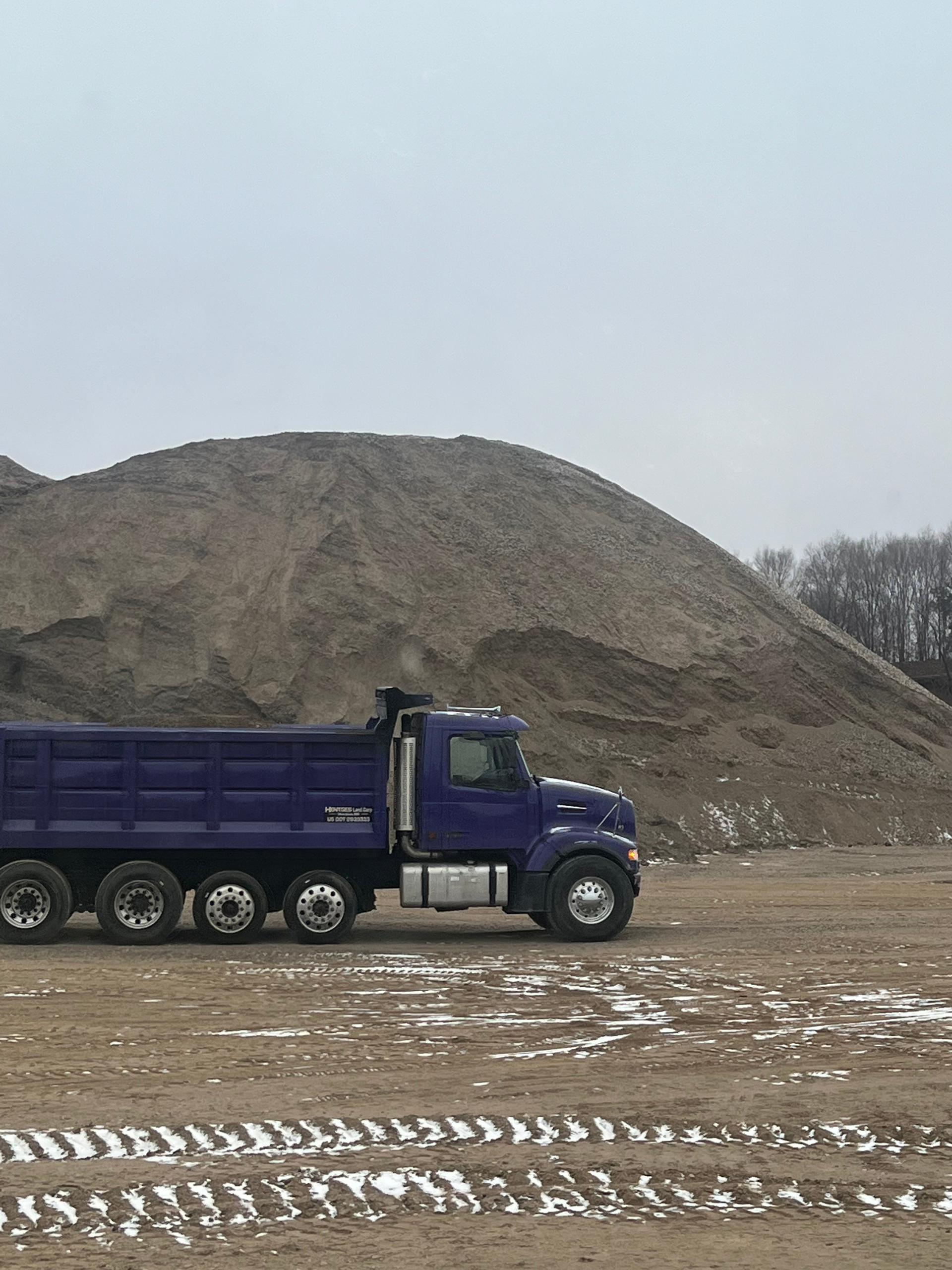 A blue dump truck is parked in front of a pile of dirt.