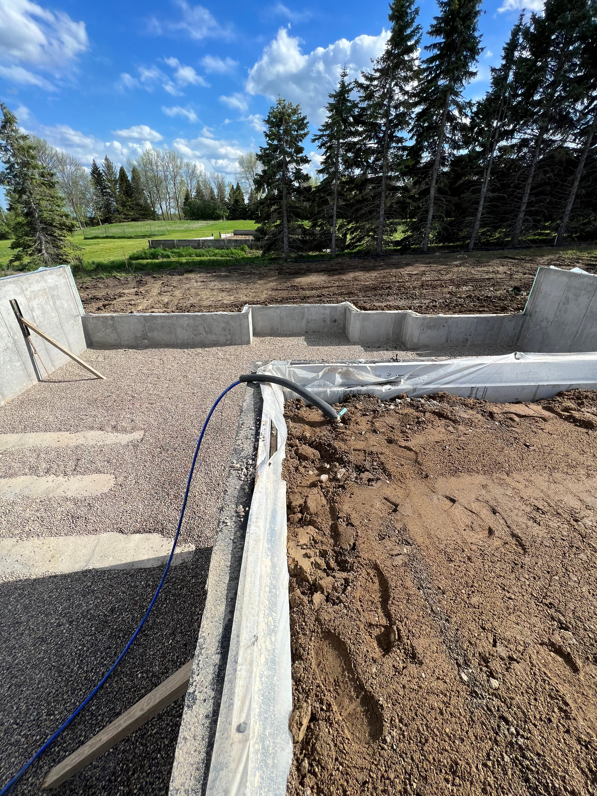 A concrete wall is being built in a dirt field with trees in the background.