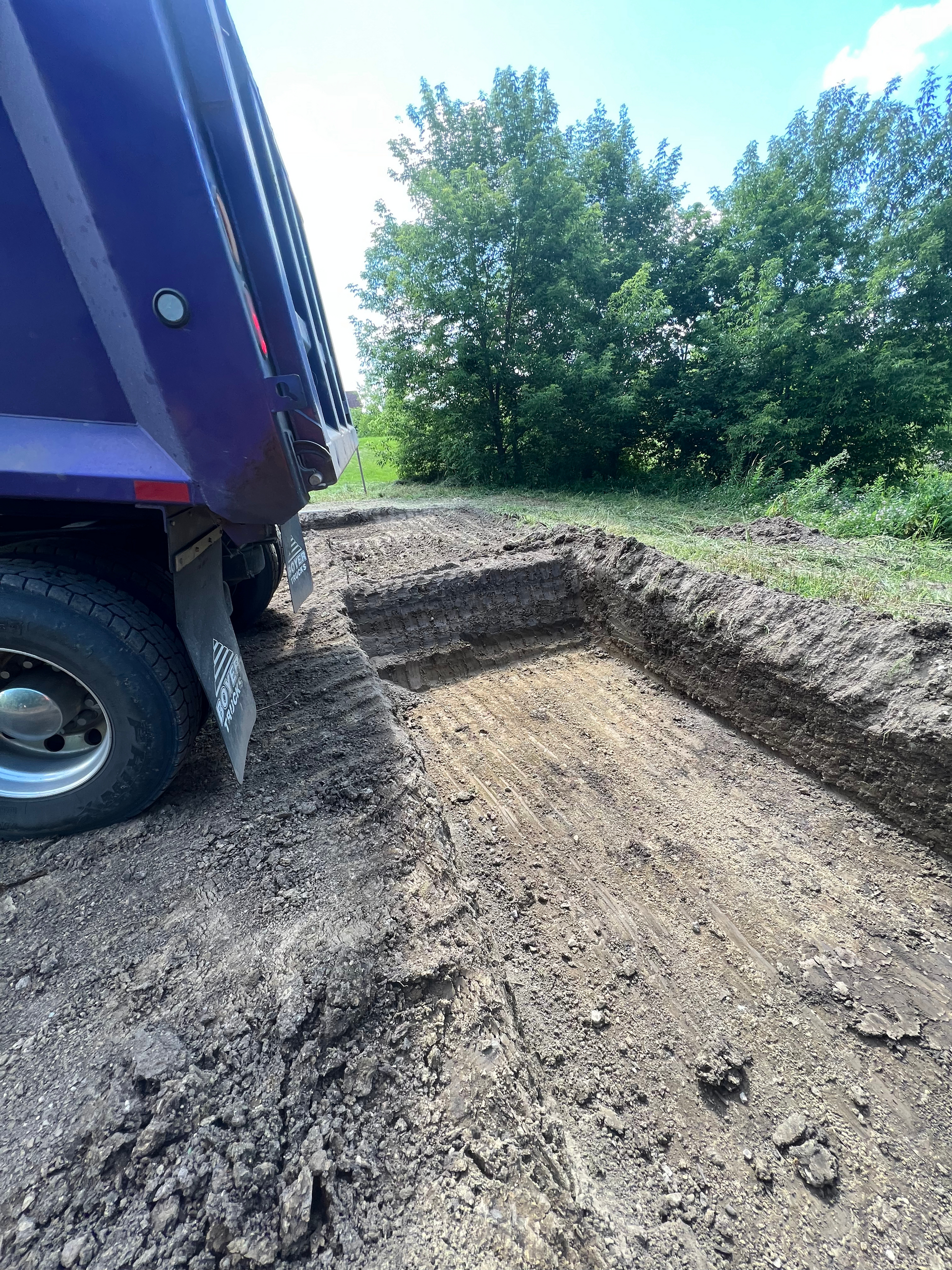 A purple dump truck is driving down a dirt road.