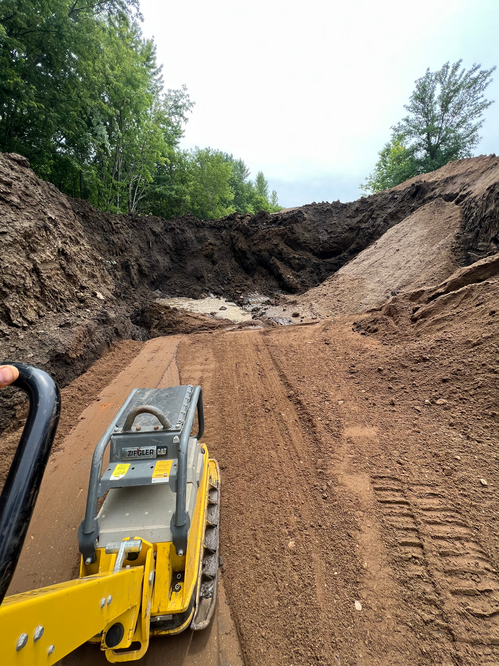 A yellow and black machine is moving dirt on a dirt road.