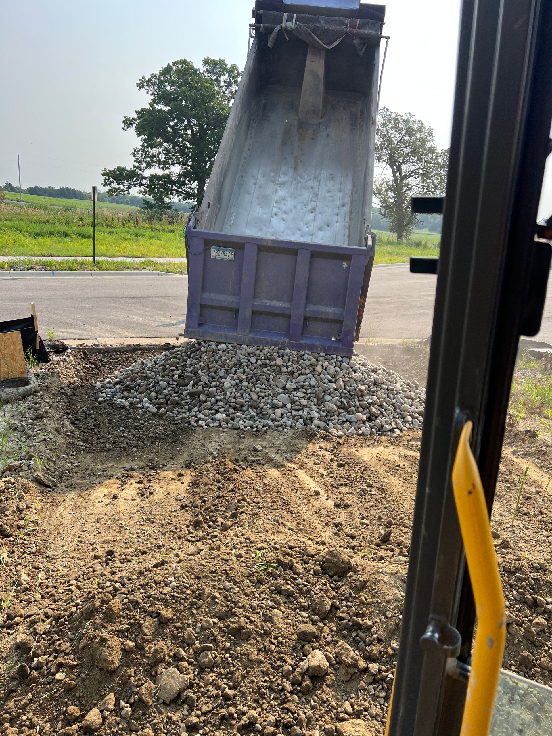 A dump truck is being loaded with gravel on the side of the road.