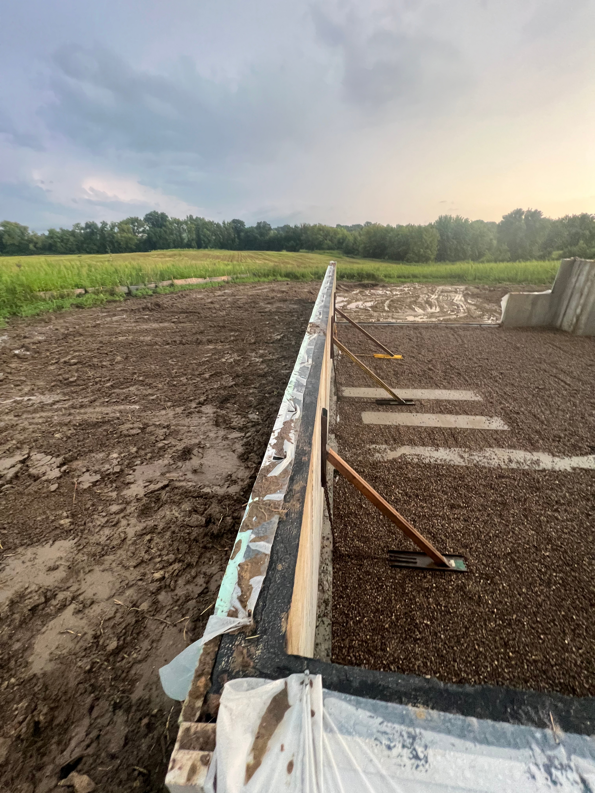 A concrete wall is being built in a muddy field.