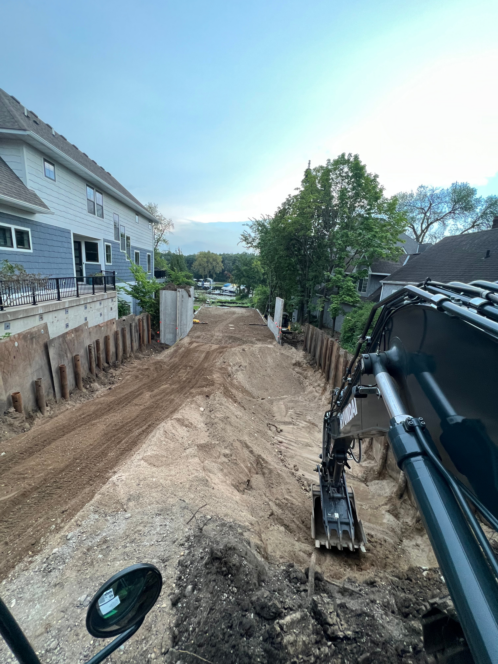 A construction vehicle is driving down a dirt road next to a house.