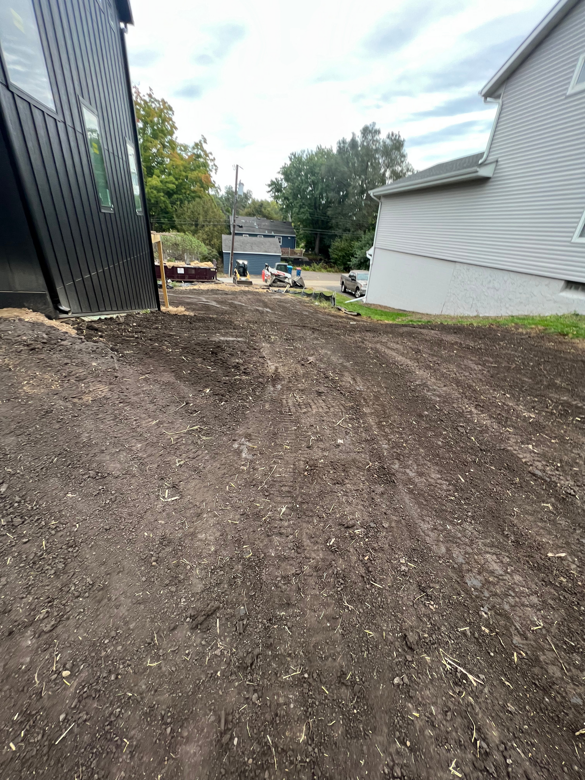 A dirt road leading to a house with a white house in the background.