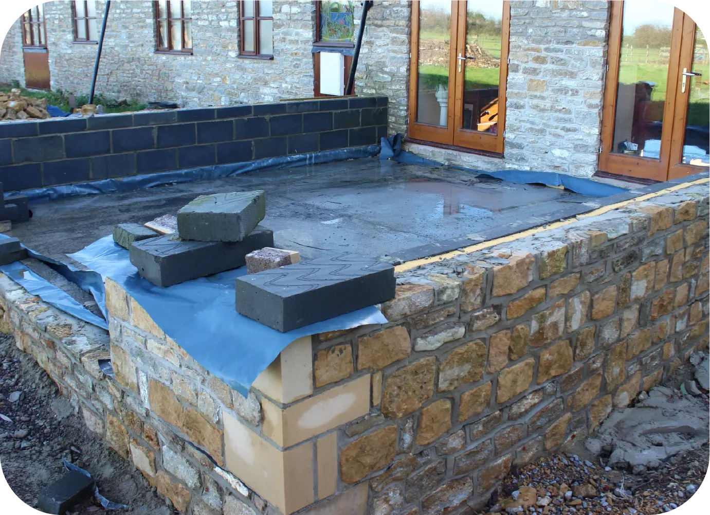 Construction of a patio, with stone walls, black bricks, and a wet concrete surface.