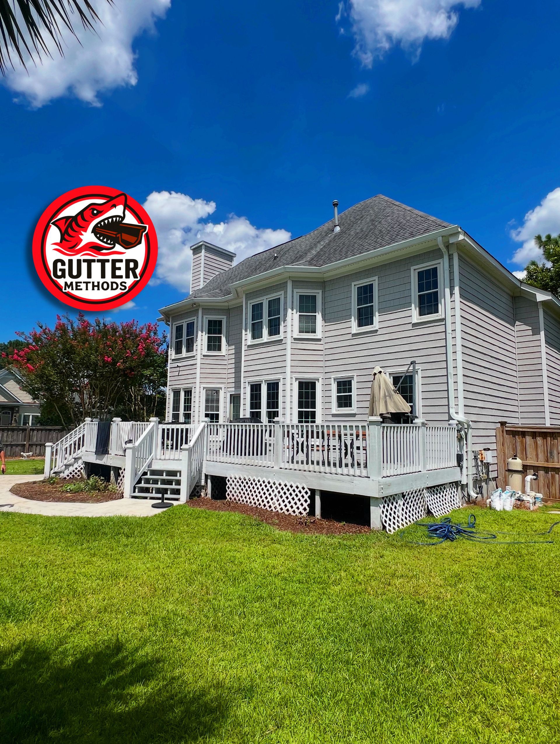 Back of a two-story house with a wooden deck, a green lawn, and blue sky; a 