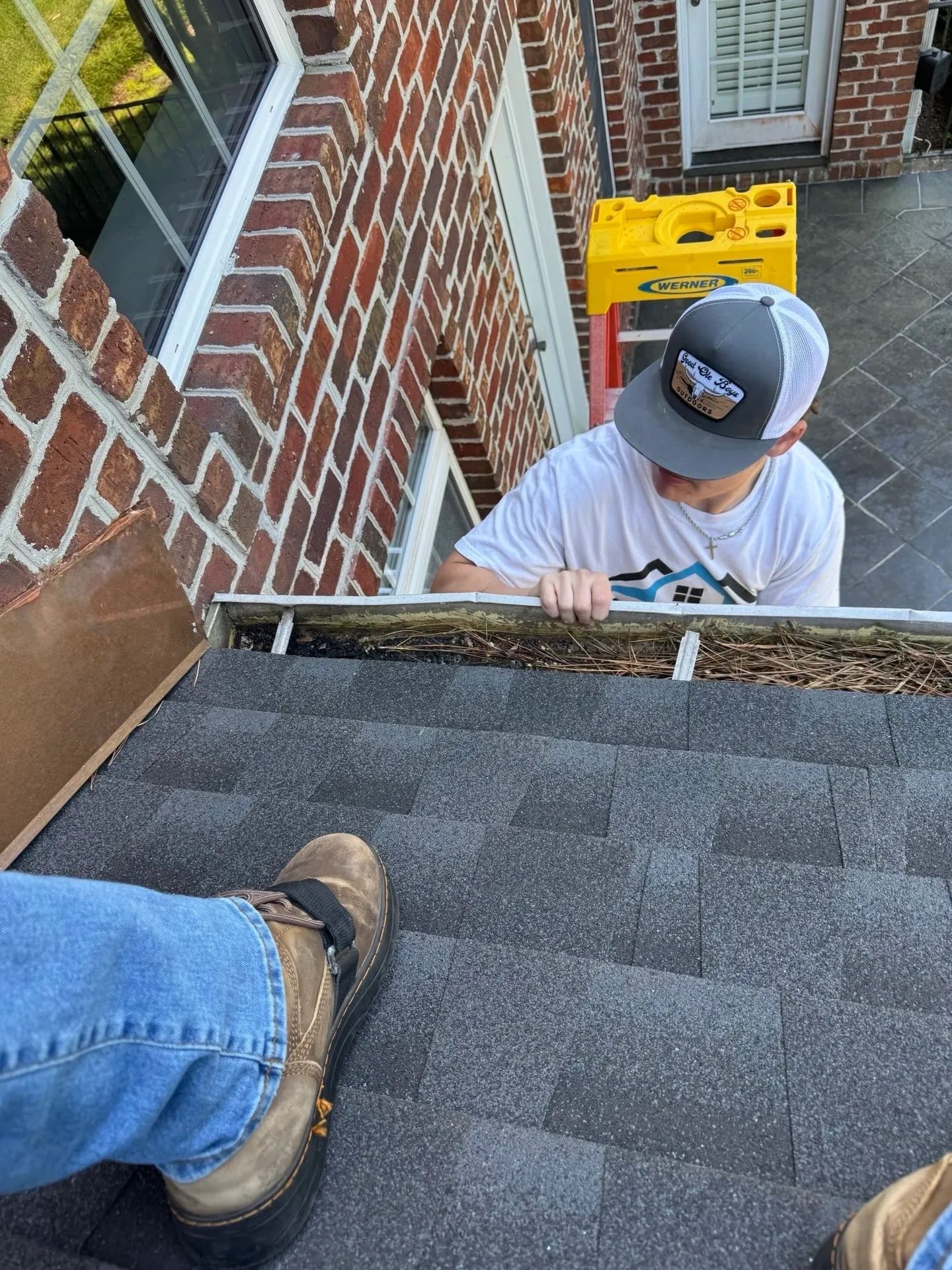 Person cleaning gutters on a brick building; seen from the roof.